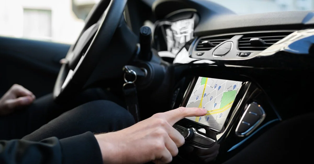 A driver using a vehicle’s touchscreen GPS navigation system to view route directions inside a luxury car.