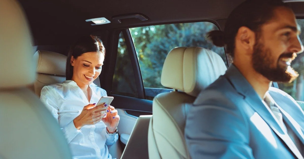 A businesswoman using her phone and laptop while traveling in a chauffeured vehicle.