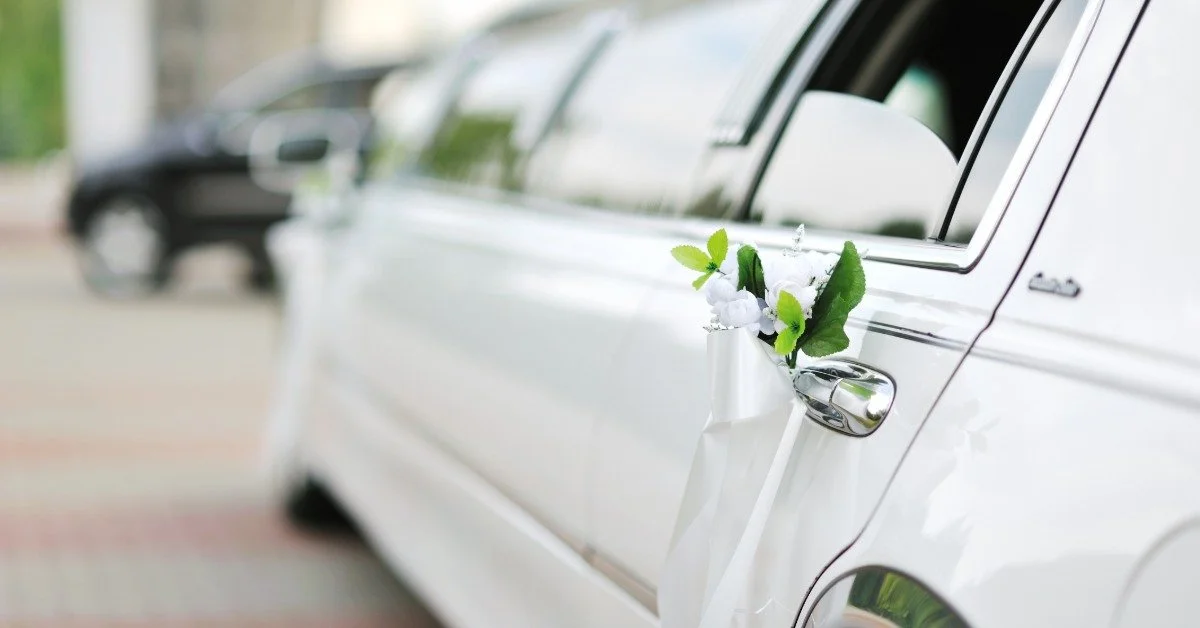A white limousine decorated with a white ribbon and small floral arrangement on the door handle.