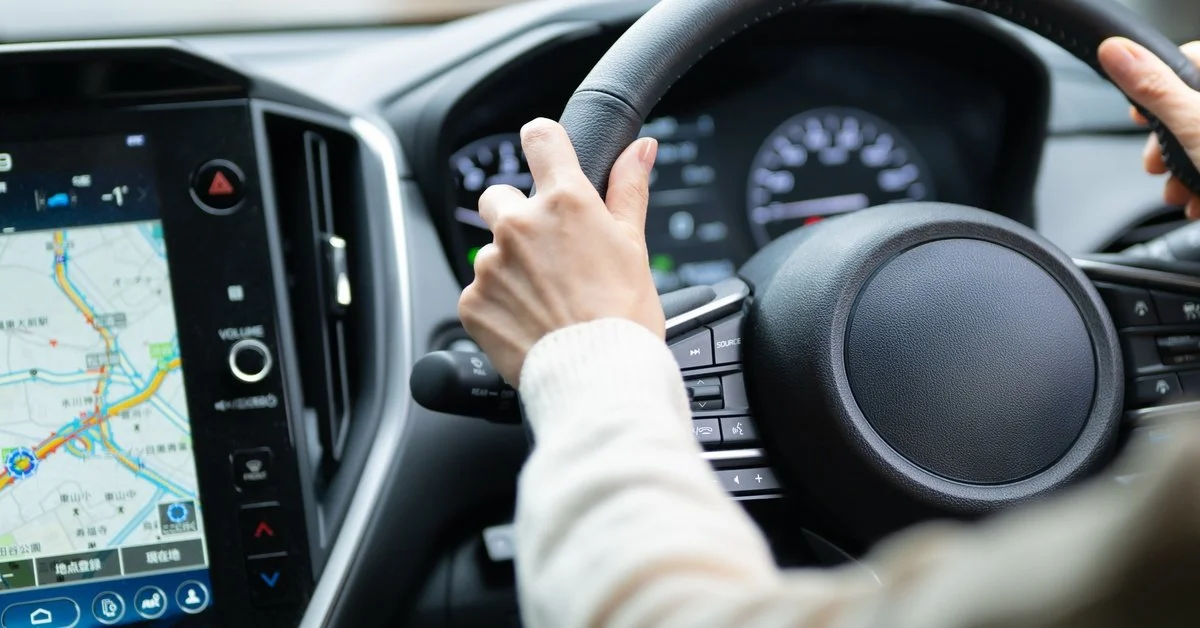 A driver holding a steering wheel while using an in-car navigation system displaying a digital map on the dashboard.