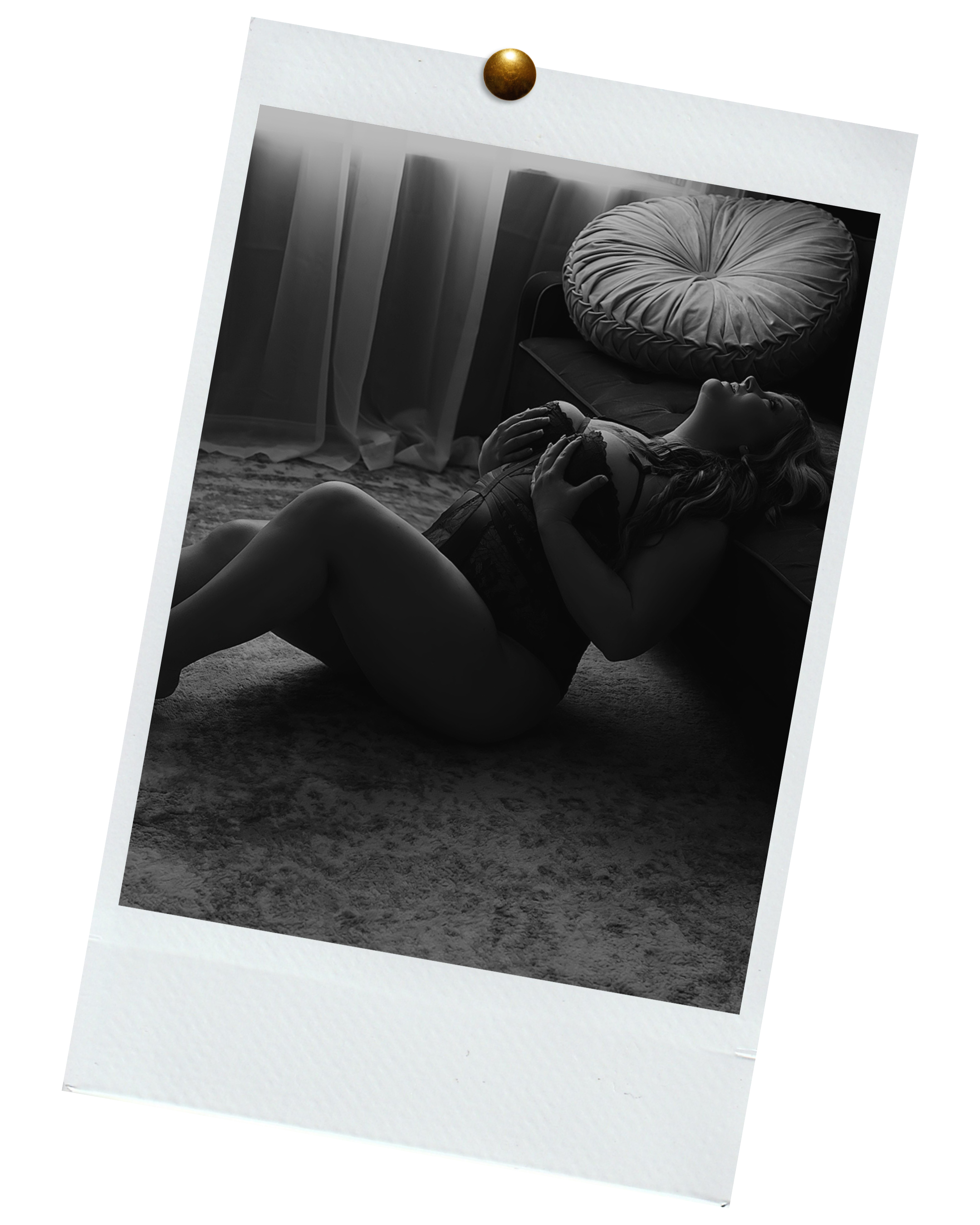 A woman lying on the carpeted floor of a room, leaning against a bed with a large pillow, in black and white photograph.