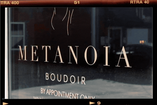 A gif showing the front door of the Metanoia Boudoir Studio, a lamp with ornate mirror in the background, and a pink neon sign.