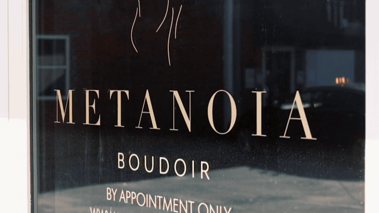 The image shows the front door of the Metanoia Boudoir studio, a 7 foot tall ornate mirror with a warm glowing lamp, and a pink neon sign that says where the magic happens..