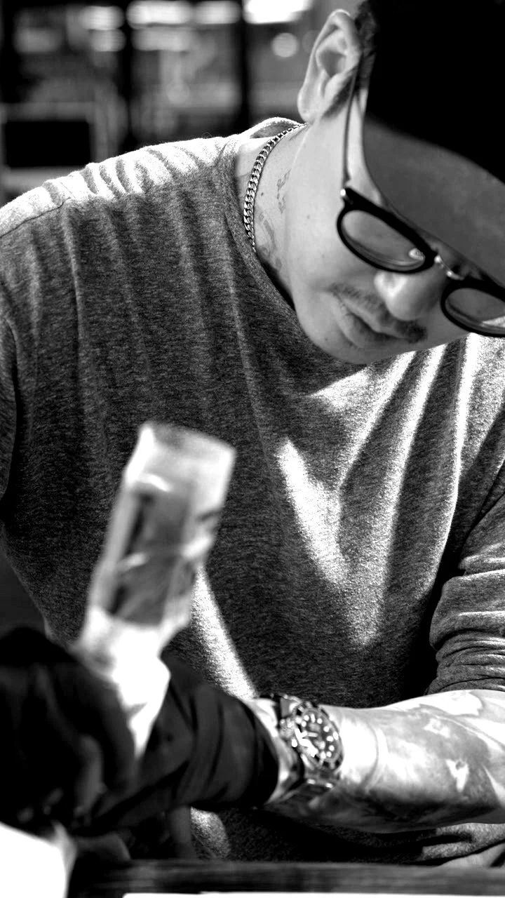 Potter - Tattoo Artist - A man with tattoos on his arm, glasses, a black cap, and black gloves is smiling while holding a fish in a black and white photo.