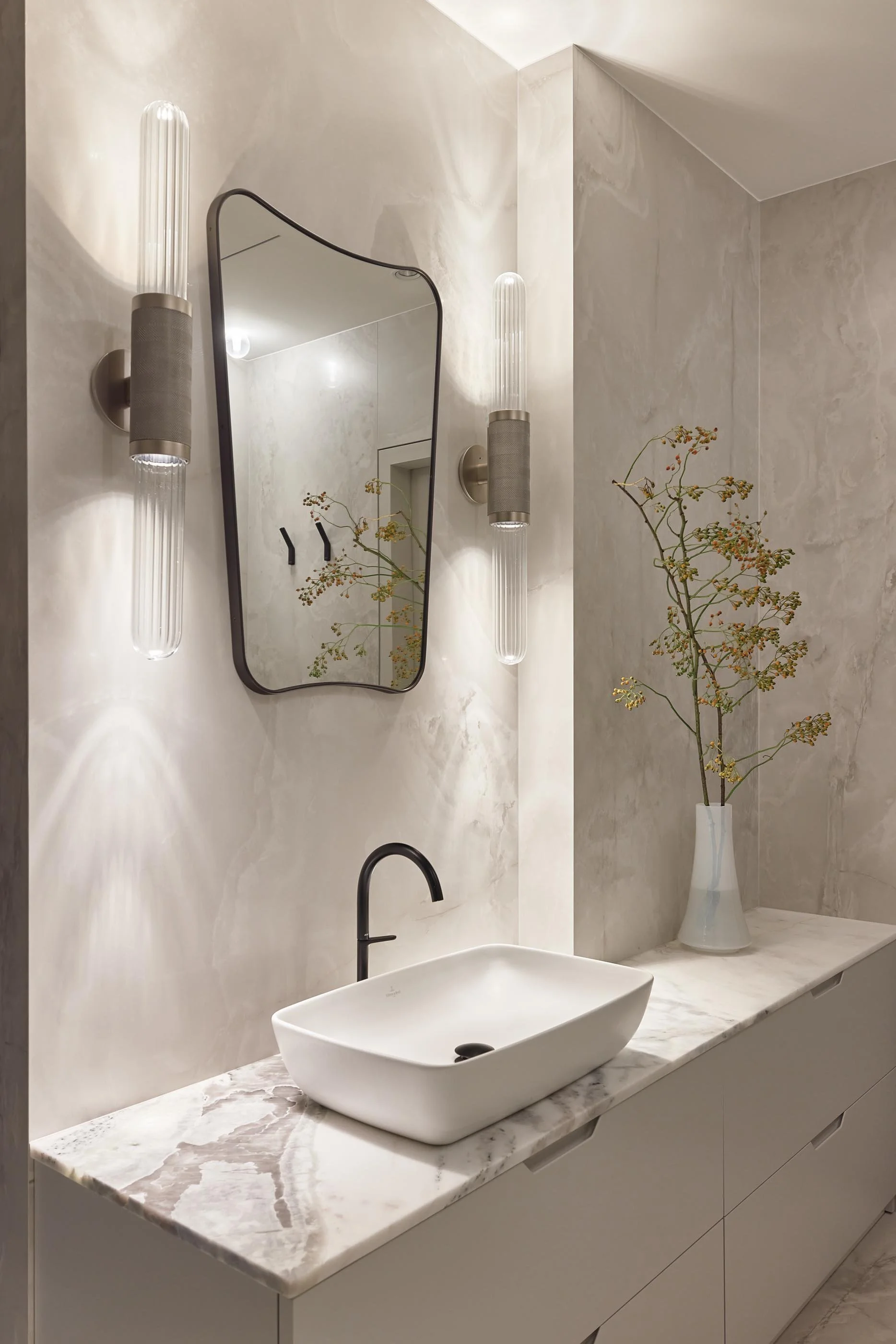 Modern bathroom with White Onyx wall tiles, freestanding bathtub, ARTICOLO light fixtures, white sink on a Oyster White marble countertop.
