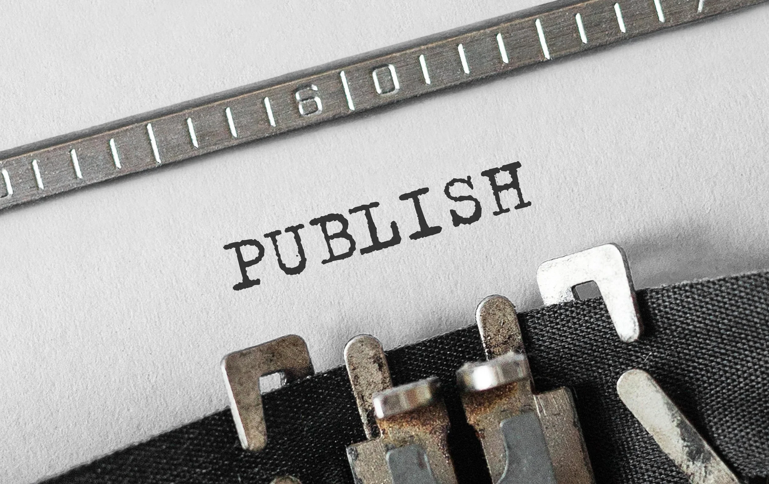 The word 'PUBLISH' appears in capital letters on a typewritten page at an angle, with the typewriter ribbon visible.