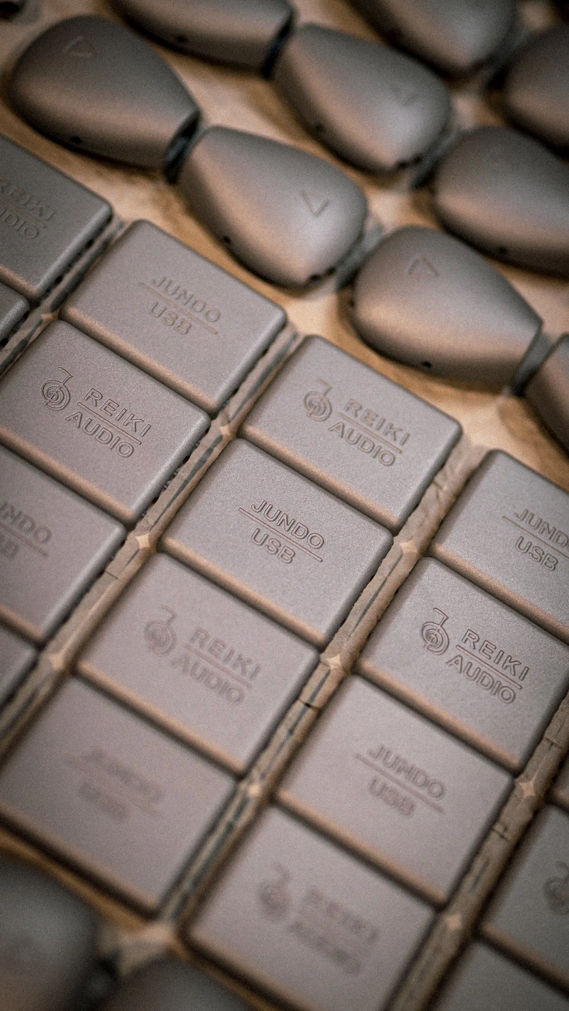 A close-up of multiple grey audio interfaces and USB hubs labeled 'REIKI AUDIO' and 'JUNDO USB', arranged in a grid pattern.