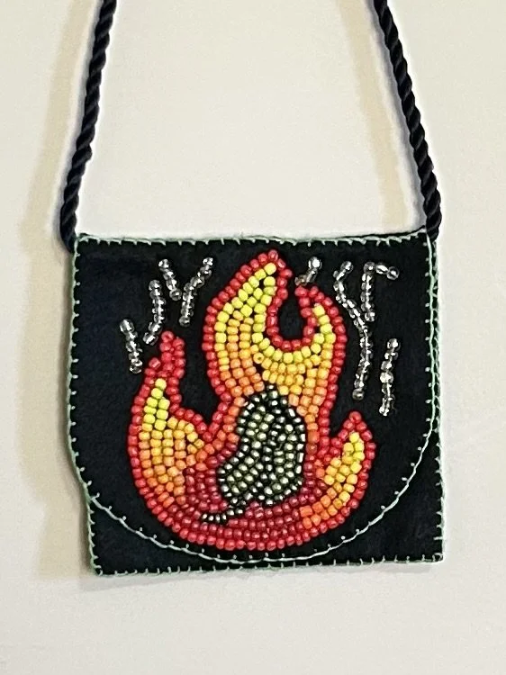 Bright beadwork on a small, black pouch portrays a fire with a green leaf in the middle of the flames.