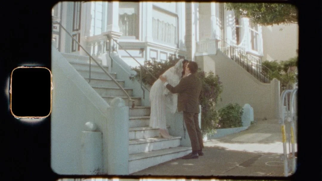 Newlyweds kiss in front of a set of stairs in wedding attire at the Painted Ladies in San Francisco, California.