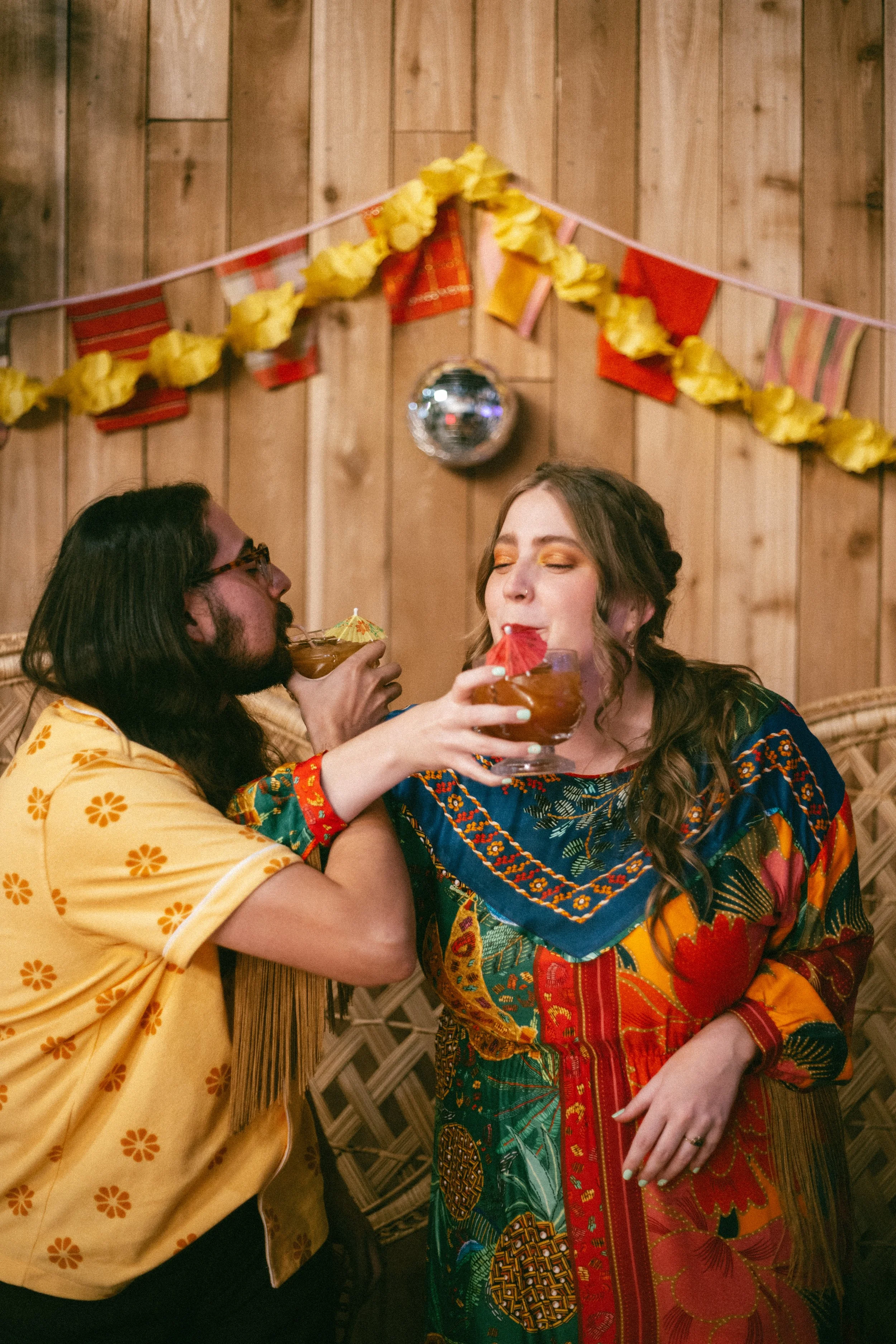 A newlywed couple toast during their wedding reception in funky attire with a dico ball in the background.