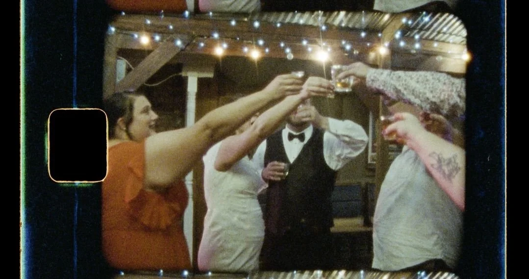 attendees of a wedding are taking shots together during the wedding reception. The newlyweds are in the center.