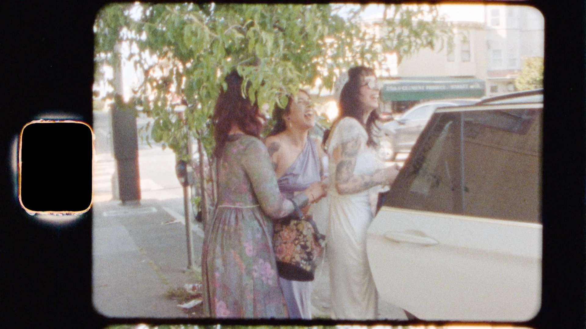 Three women laughing while changing at a car after one of the womens wedding ceremony. One of the women is wearing white and they are in San Francisco, California.