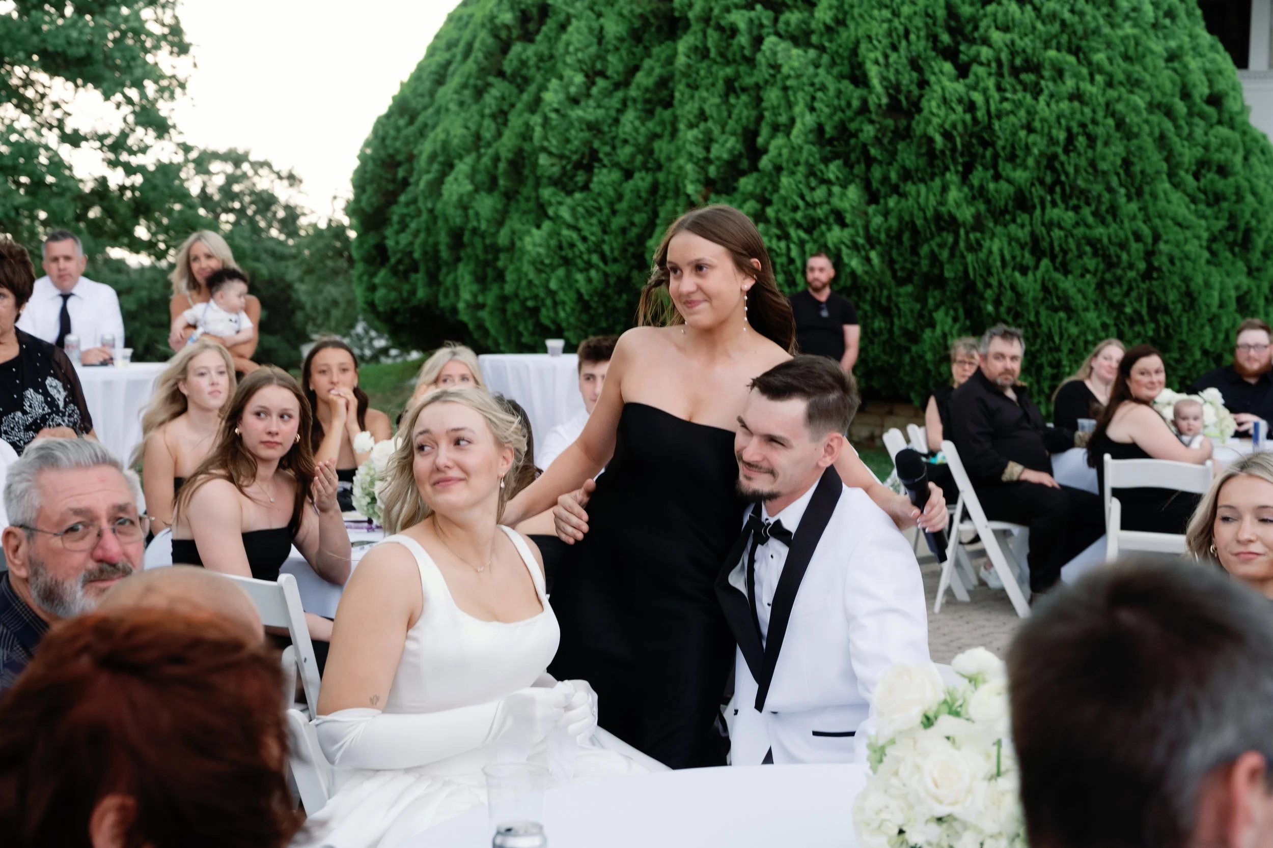 A Newlywed couple cry and smile to family members during their wedding recpetion outdoors.