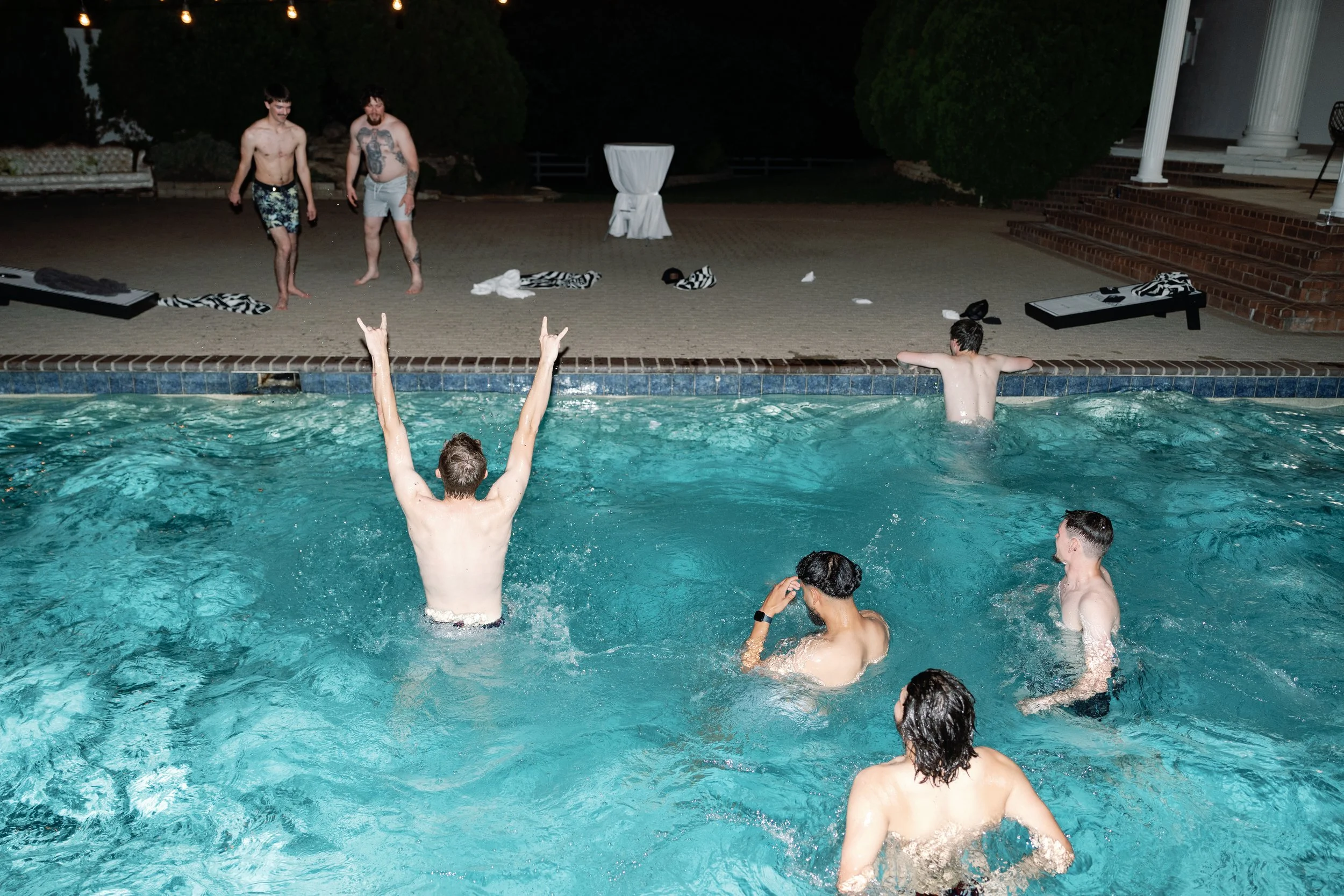 A group of men from the wedding party jump in the pool at the end of the wedding reception.