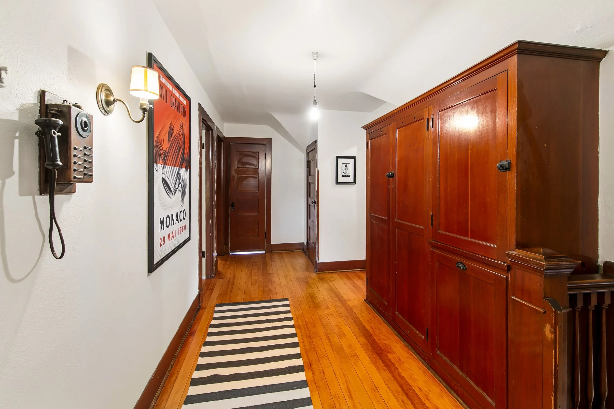 An entryway with wooden floors, a large wooden cabinet, a striped rug, and decorative wall art, including a vintage telephone on the white wall.