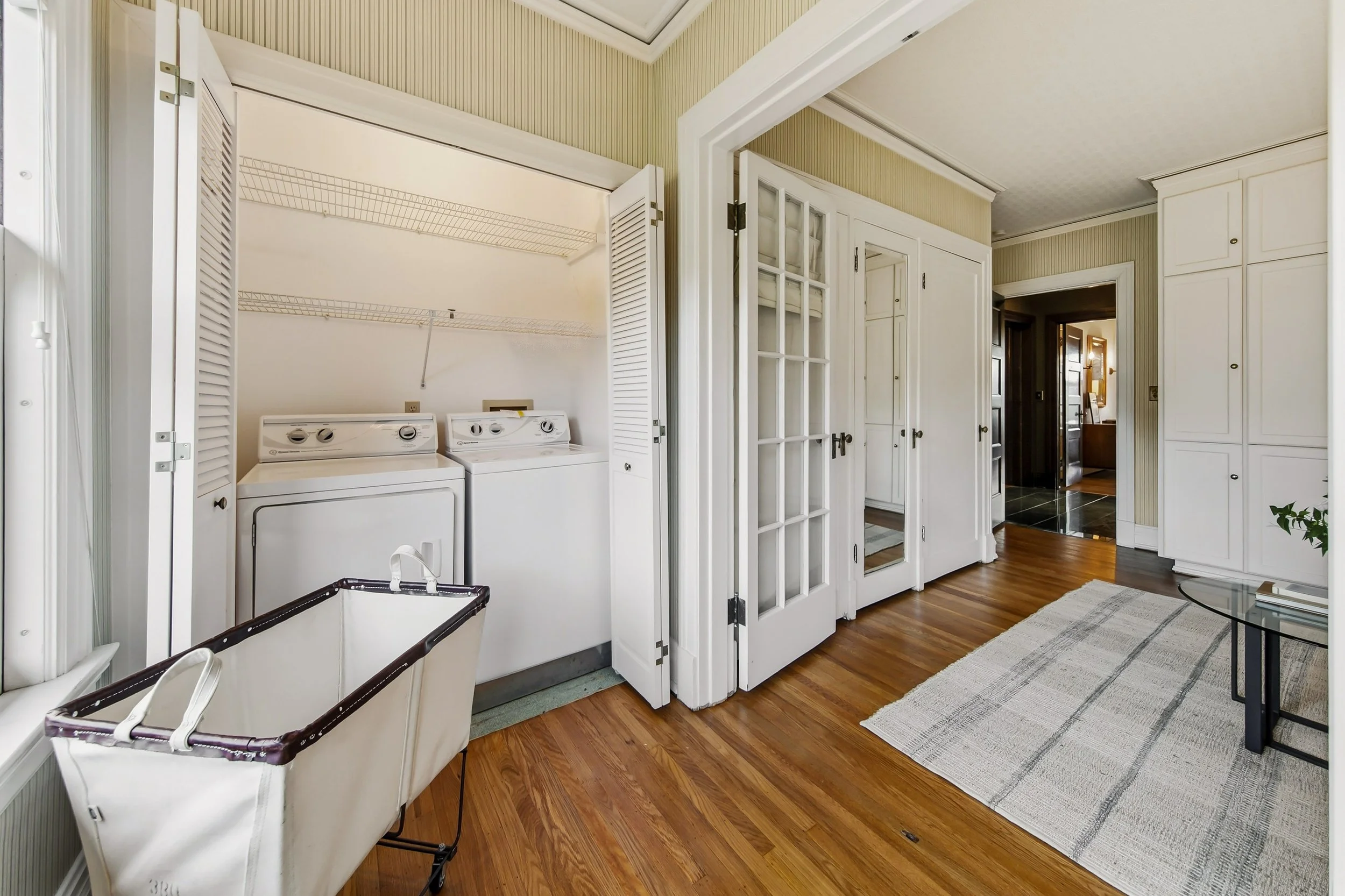 Laundry room with washer and dryer, laundry basket, white cabinets, door with glass panes, hardwood floor, and a rug.