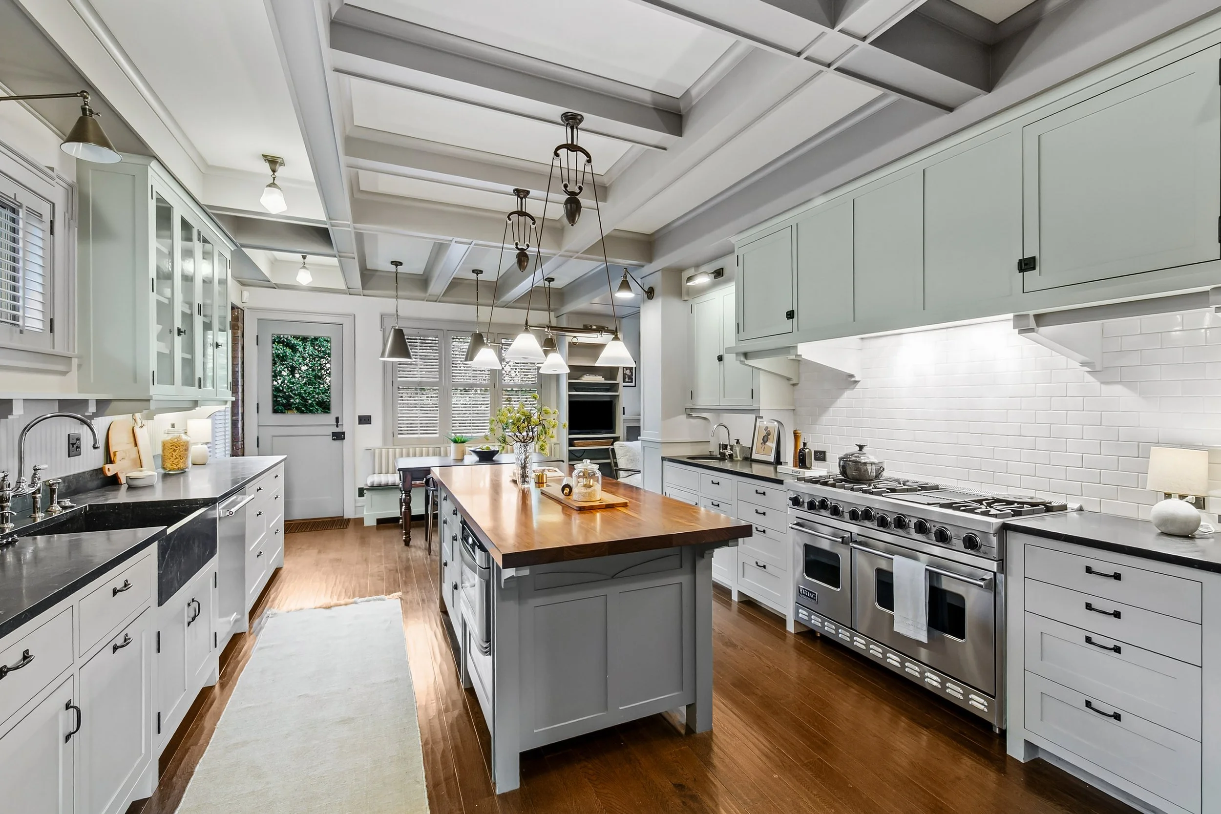 Updated white kitchen with cabinets, a wooden island, black countertops, modern appliances, pendant lights, window blinds, and hardwood floors.