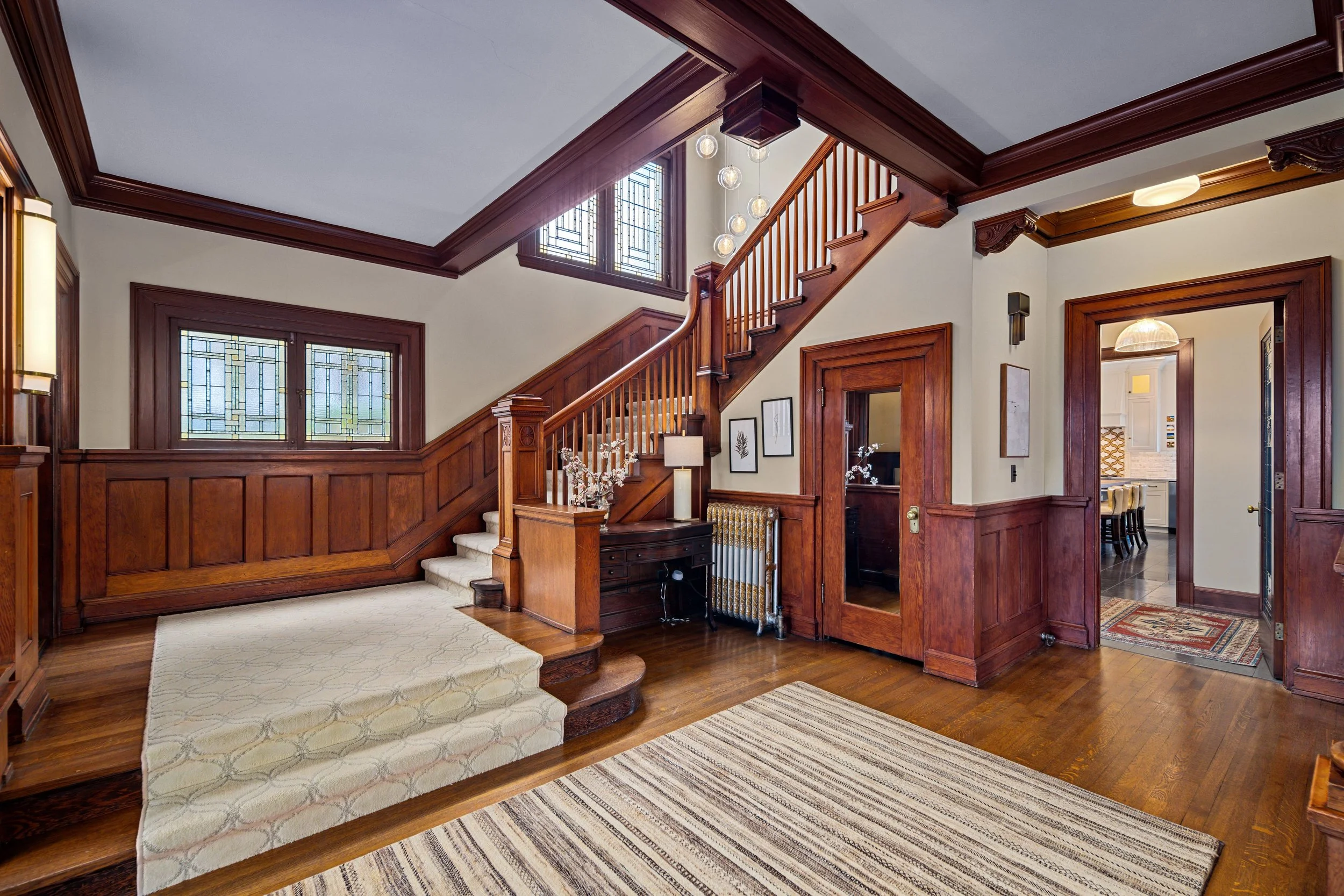 Interior of a house with wooden staircase, stained glass windows, and hardwood floors.
