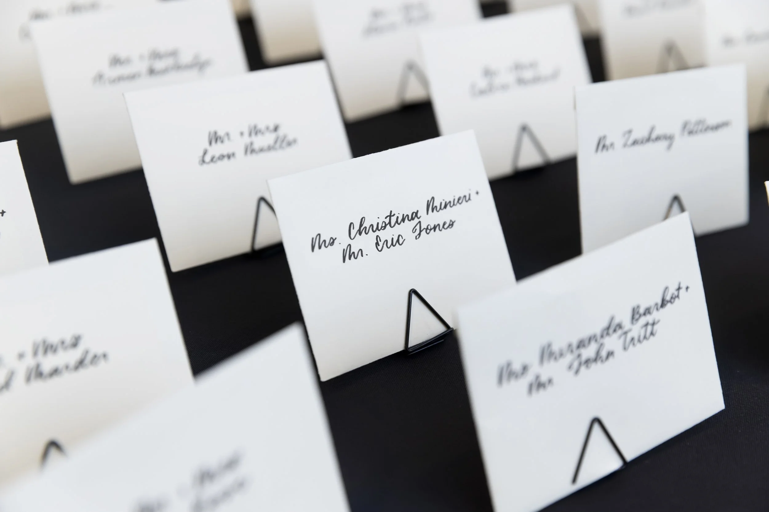 Escort cards handwritten in modern calligraphy on white envelopes, black writing at a wedding in Jersey City, NJ