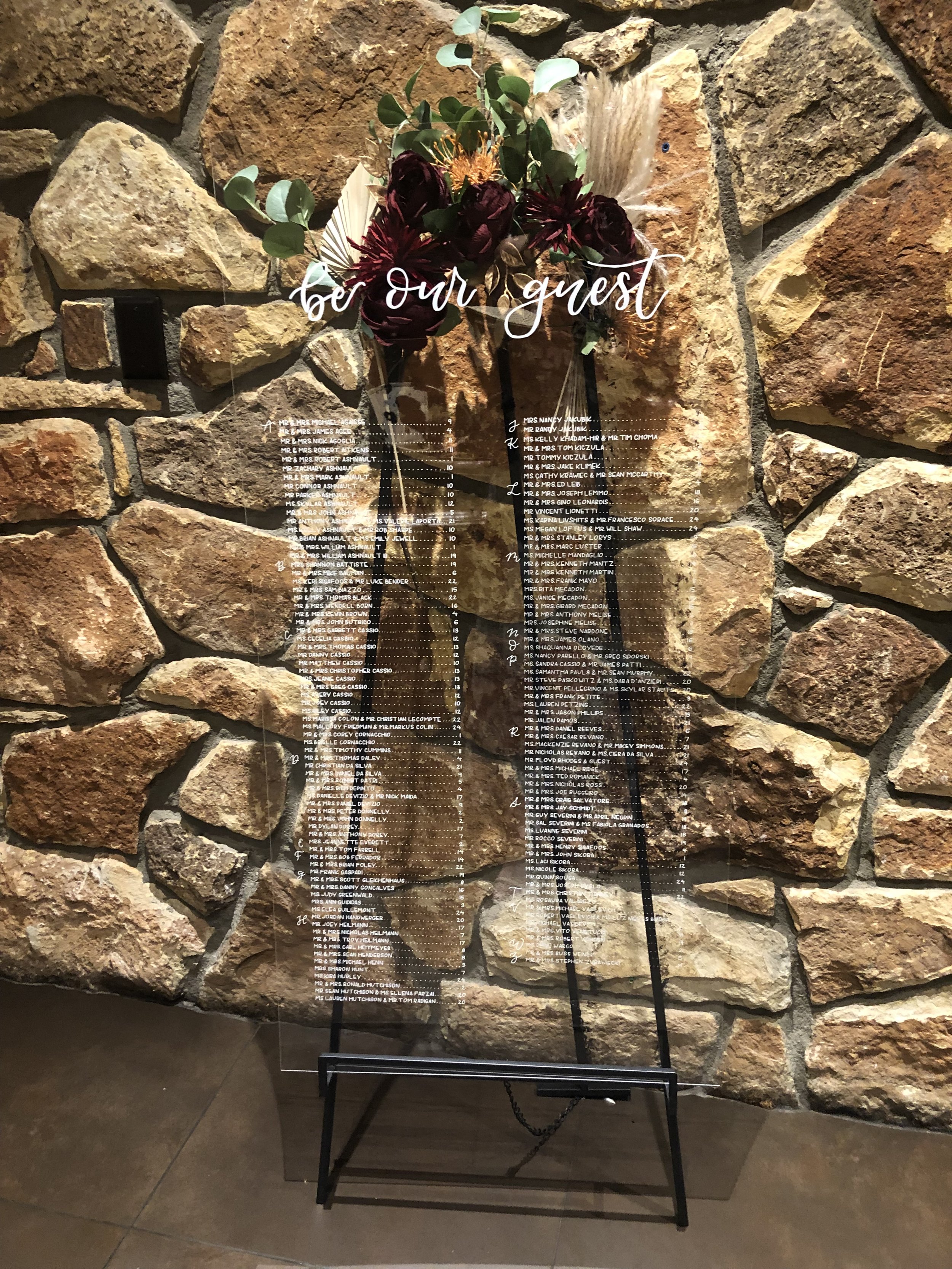 Clear acrylic seating chart with elegant calligraphy, displaying guest names and table assignments in a modern, minimalist style.