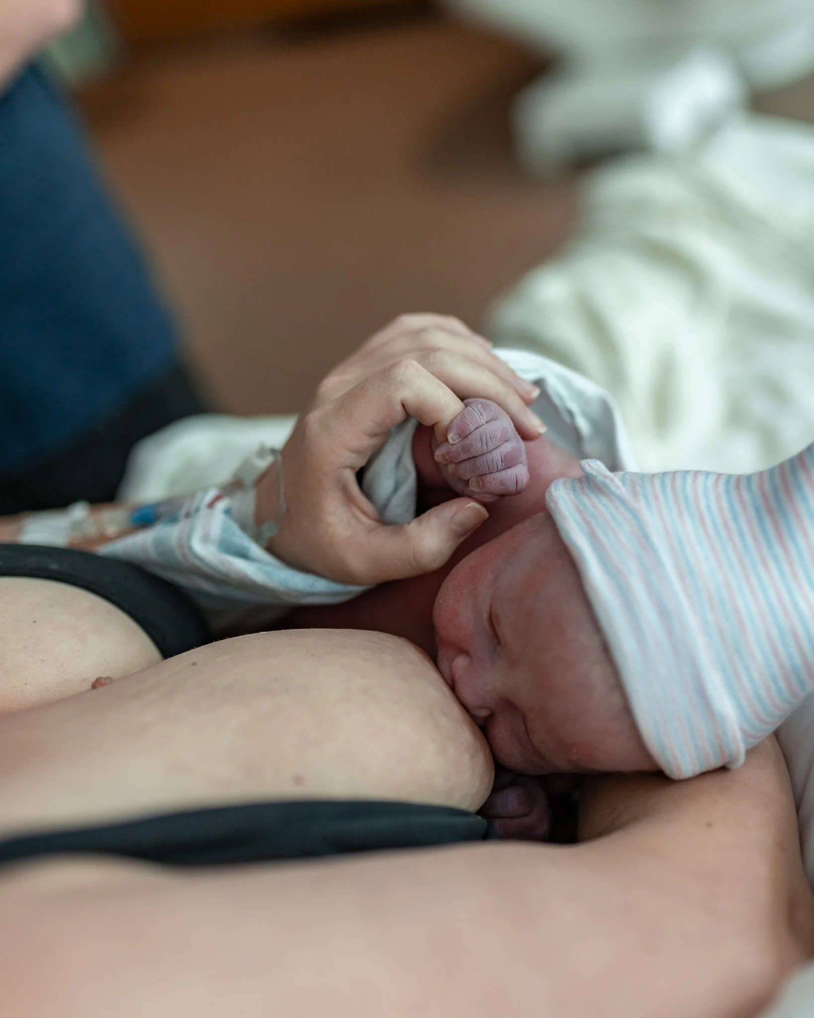Colorized photo of newborn baby breastfeeding immediately after birth. Baby is holding her mother's finger while she latches.