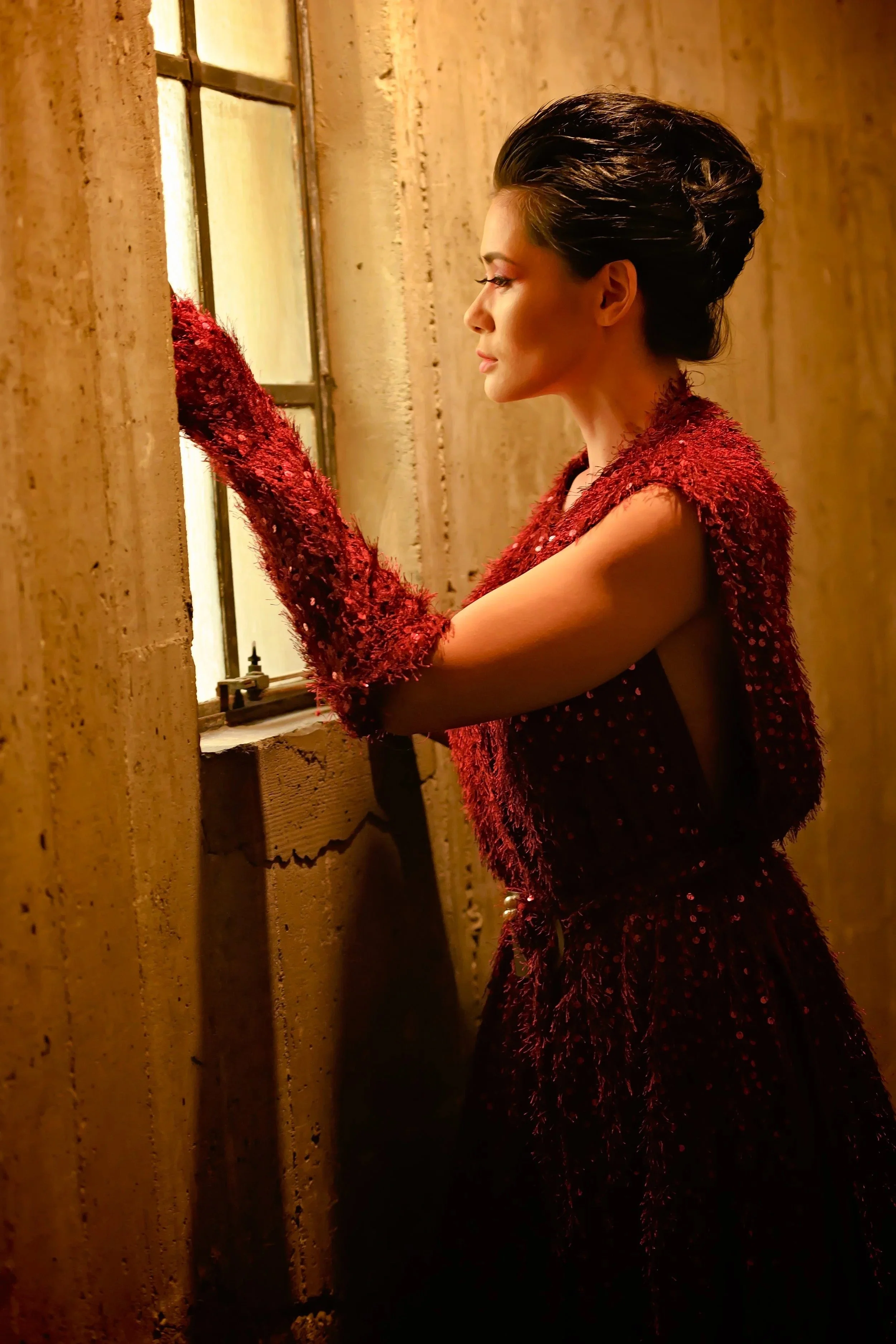Fashion portrait of a woman in a burgundy gown and long gloves by a window.