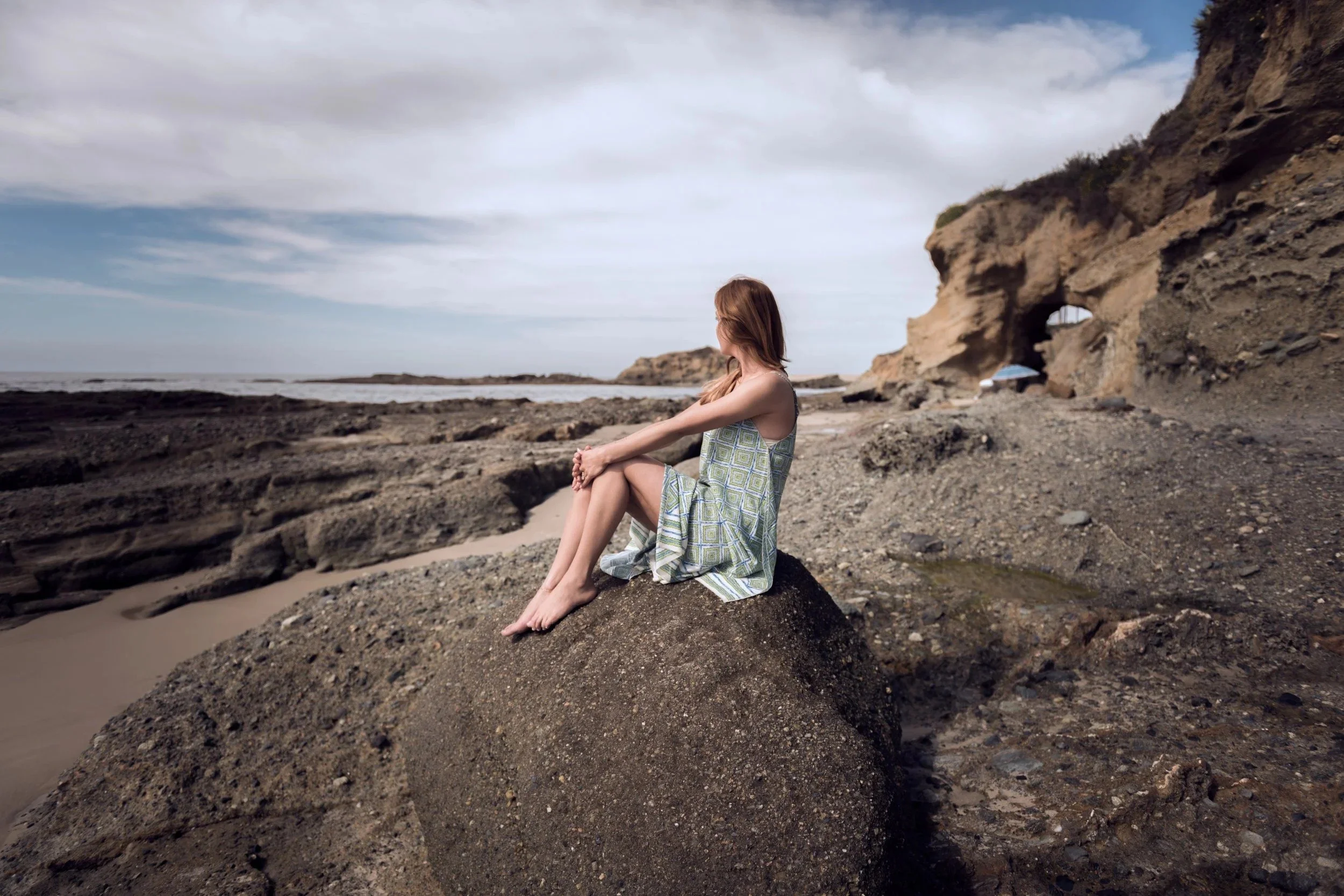 Portrait of a woman seated on rocks at a coastal cliff beach.