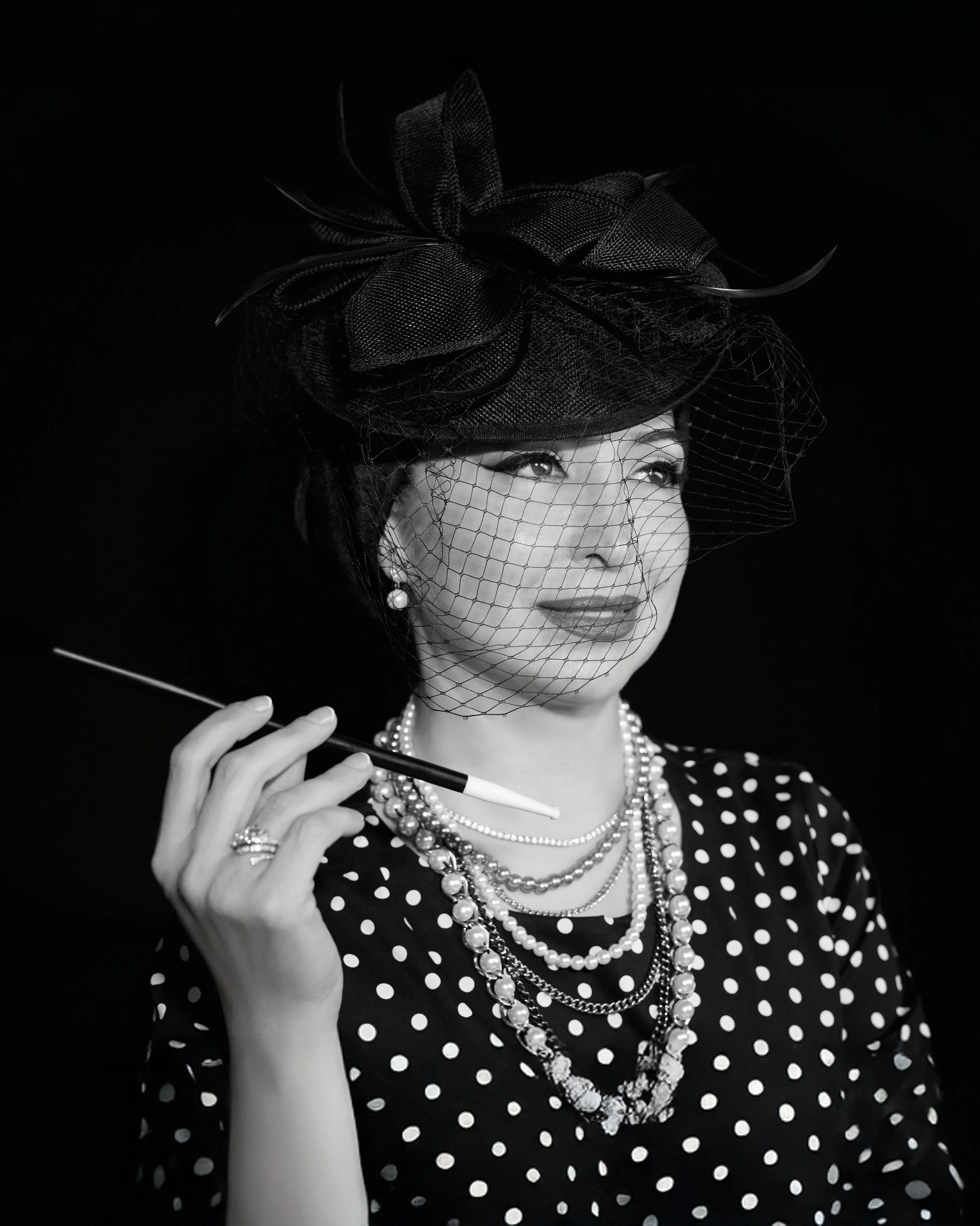 Vintage-styled black-and-white portrait of a woman in a veiled hat and pearls