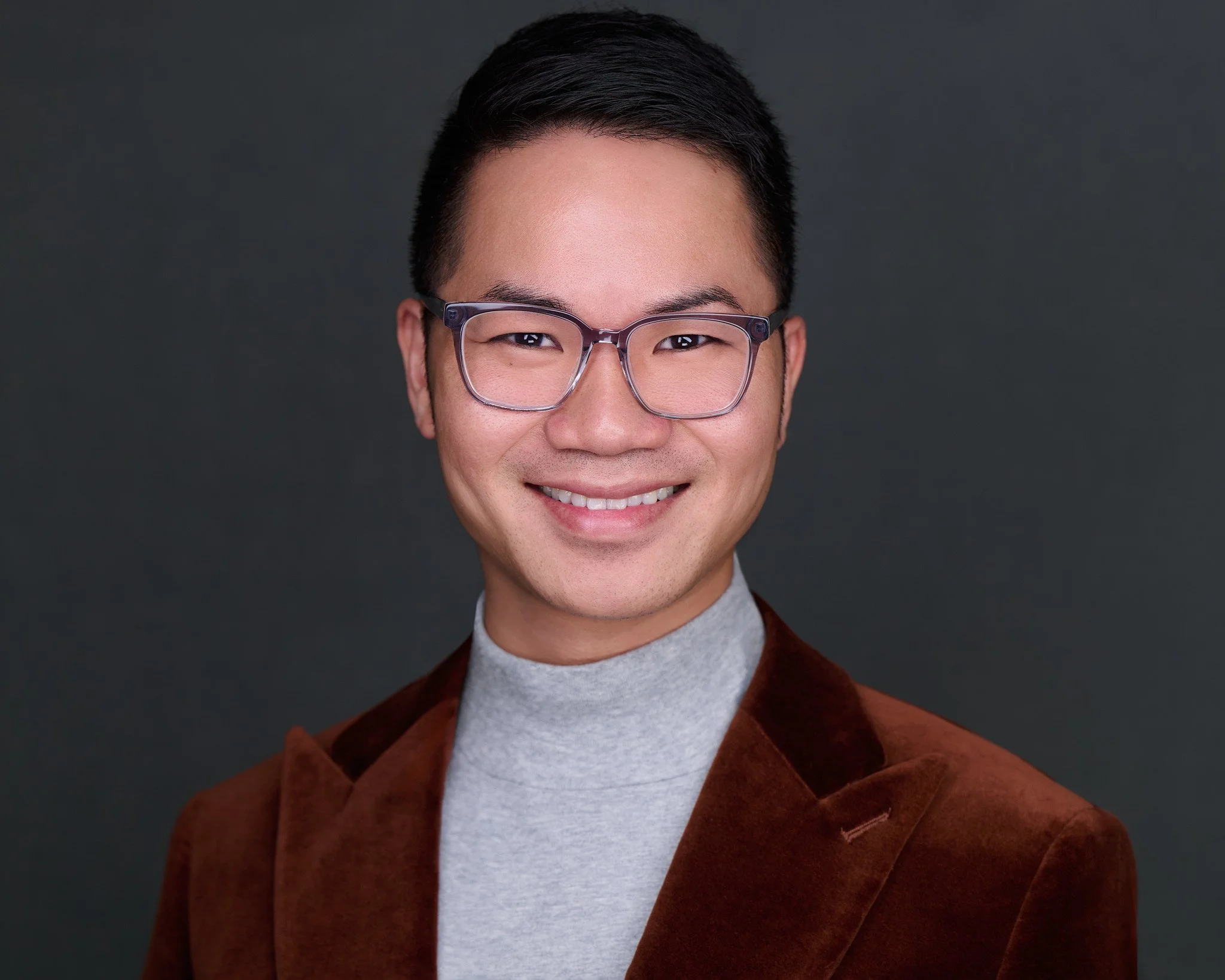 Corporate headshot of a man in glasses and a rust velvet blazer on a charcoal backdrop, Orange County team headshot session