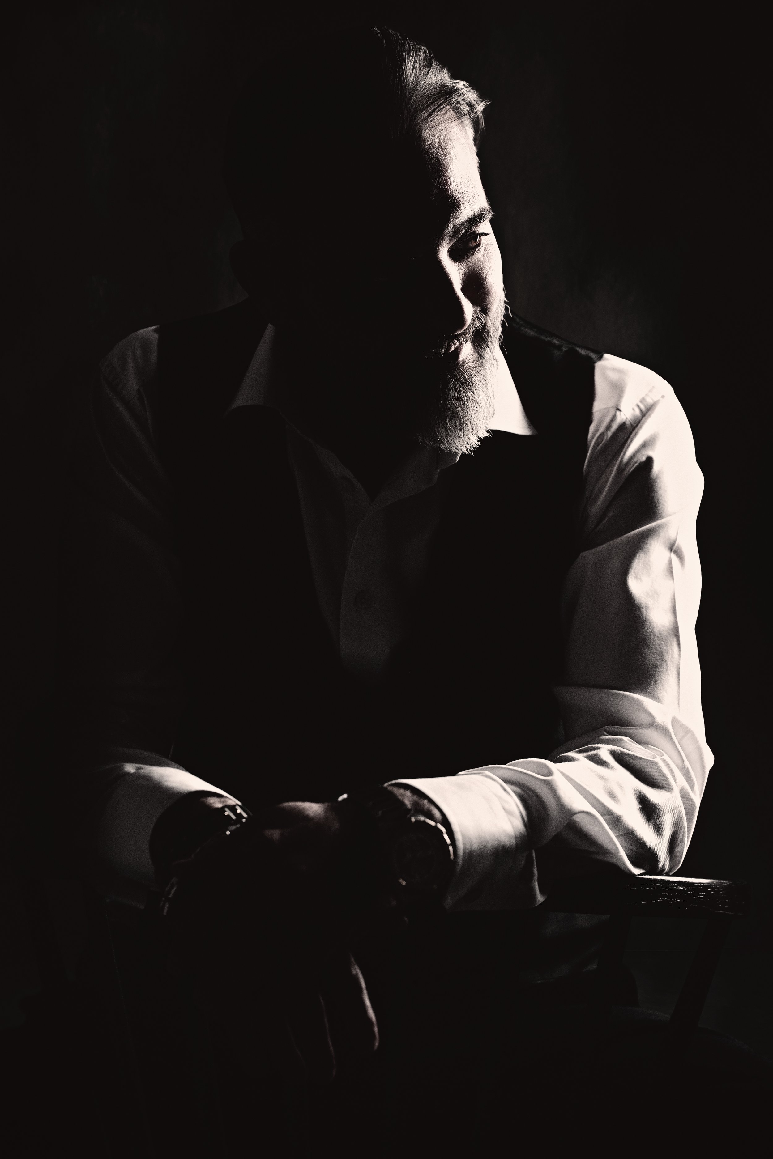 Low-key portrait of a bearded man seated in dramatic side light