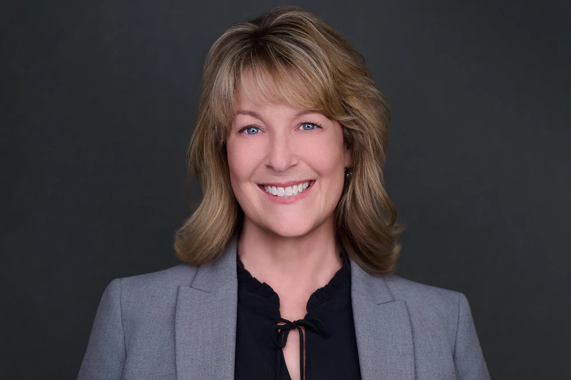 Corporate headshot of a woman in a gray blazer on a charcoal backdrop, Orange County team headshot session