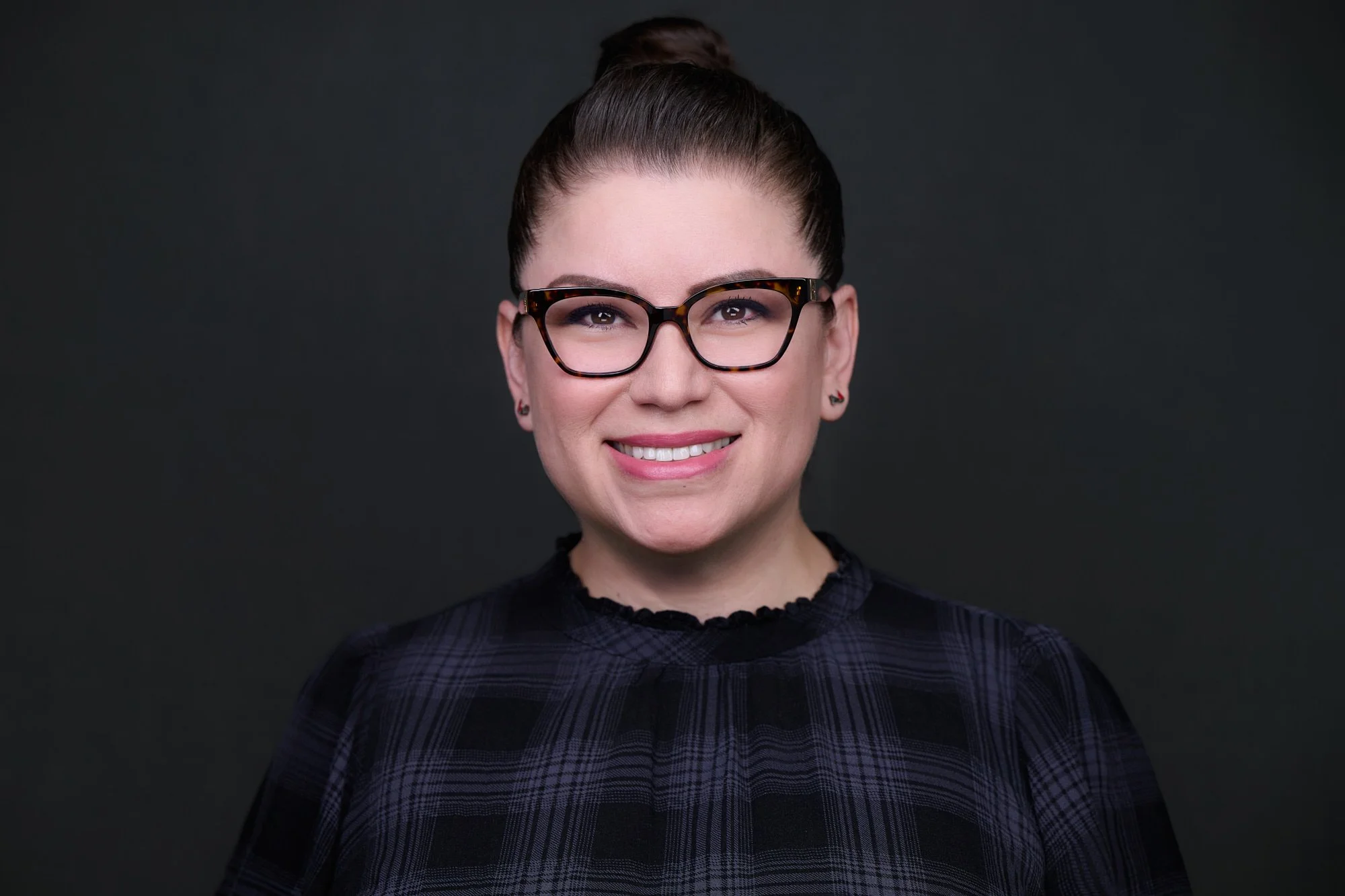 Corporate headshot of a woman with glasses in a dark plaid top on a charcoal backdrop, Orange County team headshot session