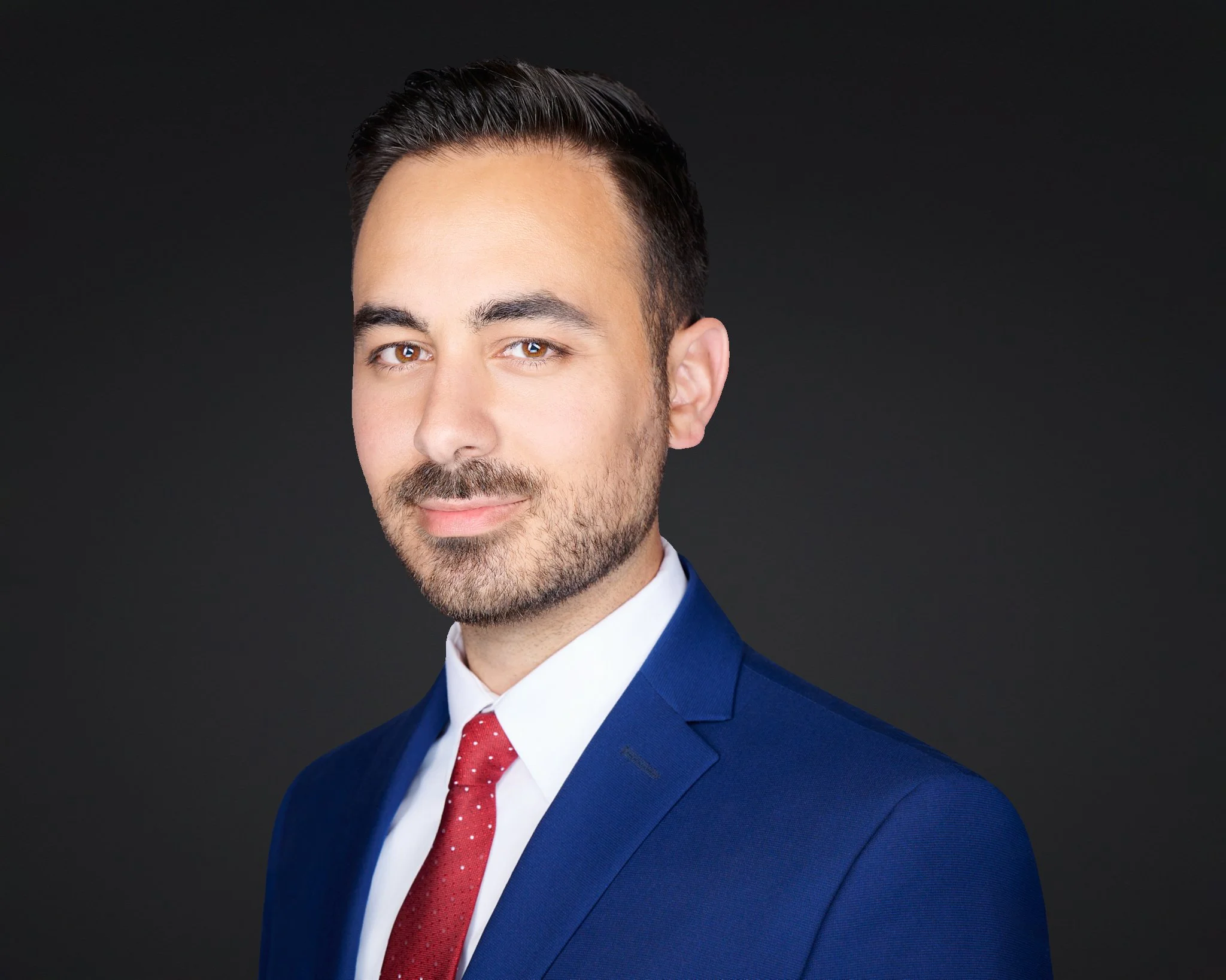 Business headshot of a man in a navy suit and red tie on a dark background.