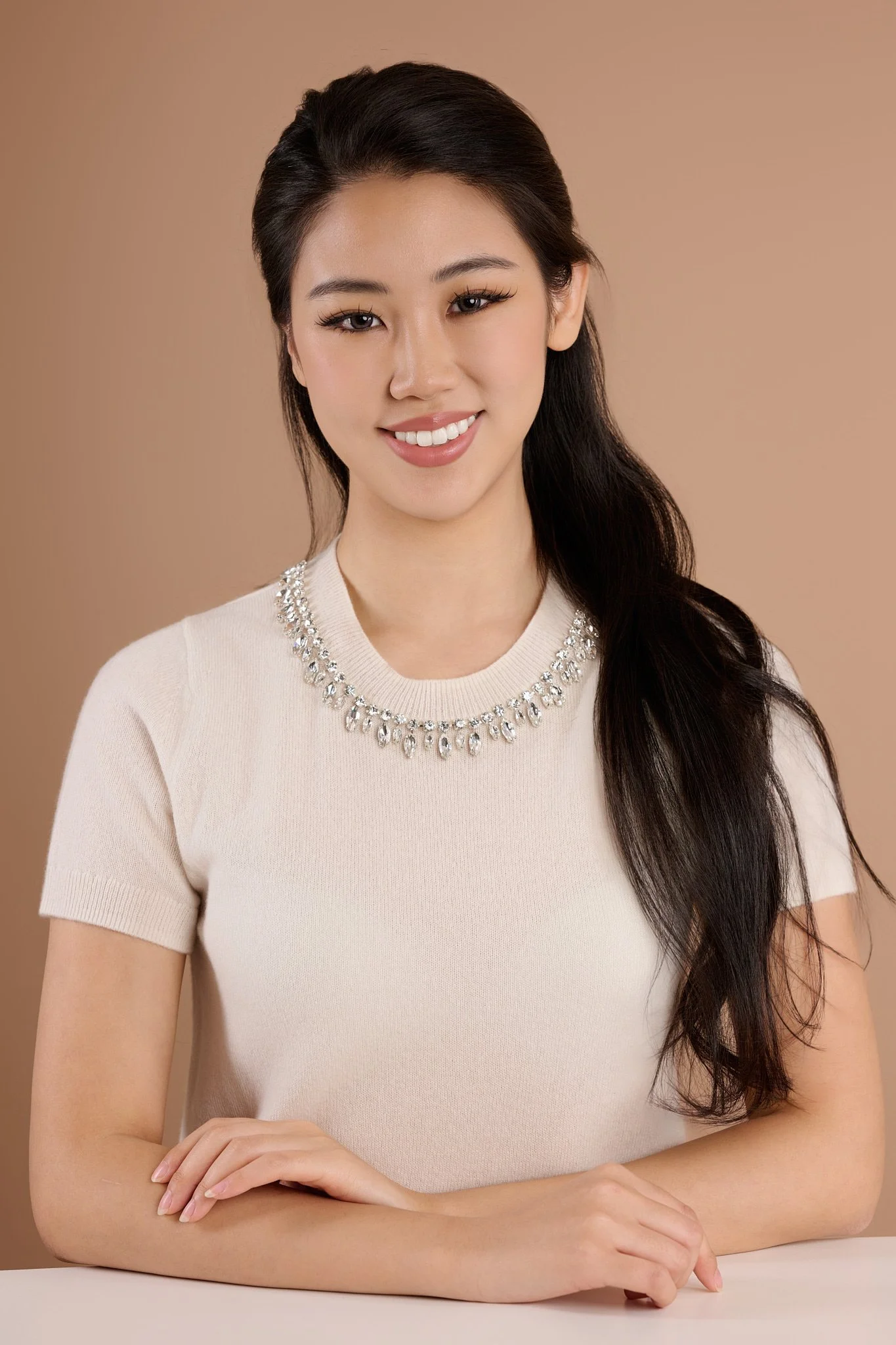 Studio portrait of a smiling woman in a white top with a jeweled neckline