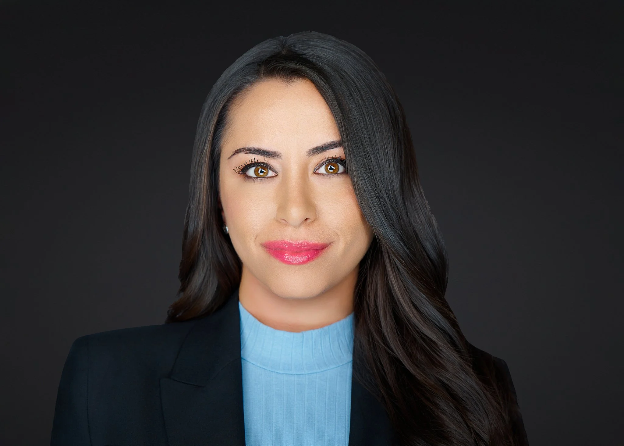 Attorney headshot of a woman in a black suit and blue blouse against a dark gray studio background, Irvine, Orange County