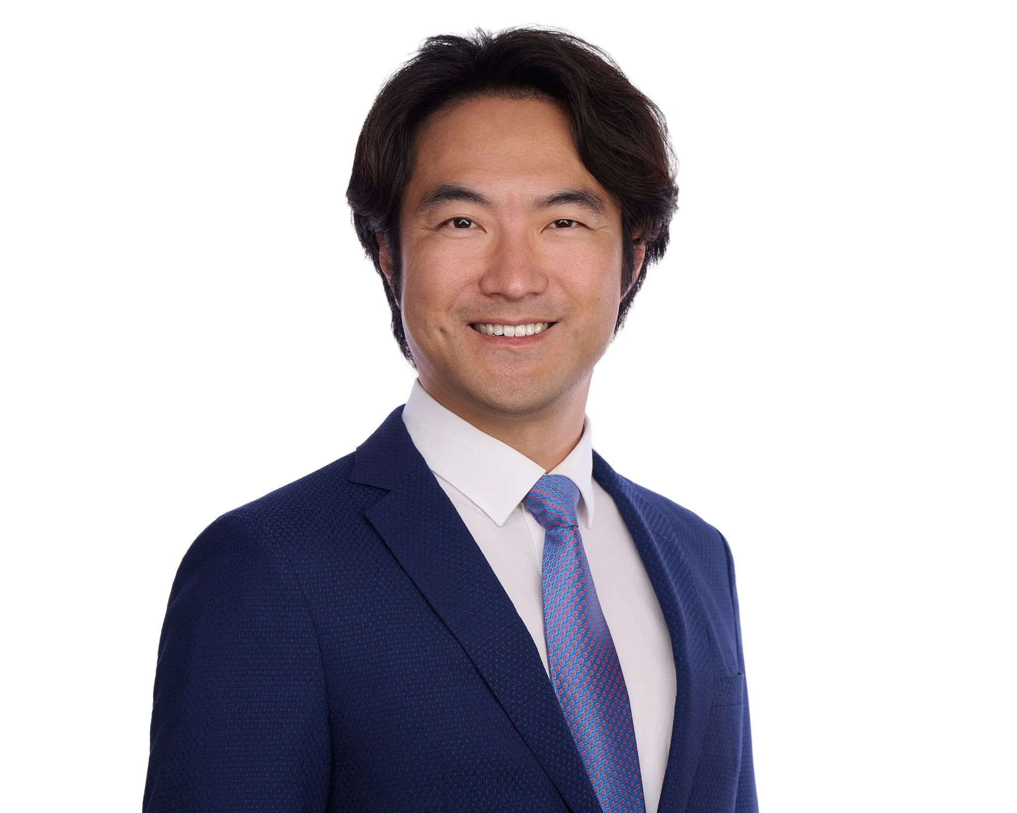 Executive headshot of a man in a navy suit and blue tie, photographed on a white background.