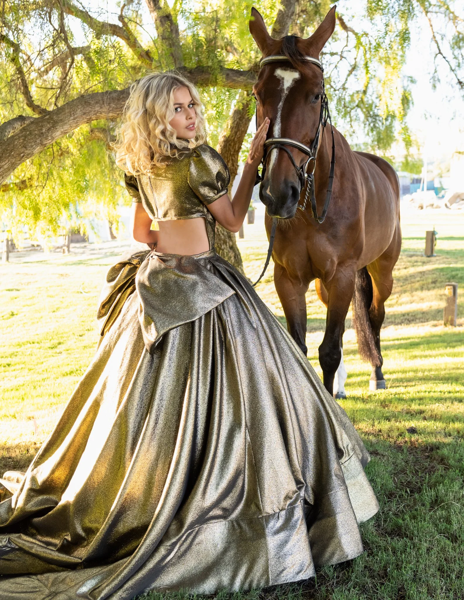 Portrait of a woman in a gold gown standing beside a horse under a tree
