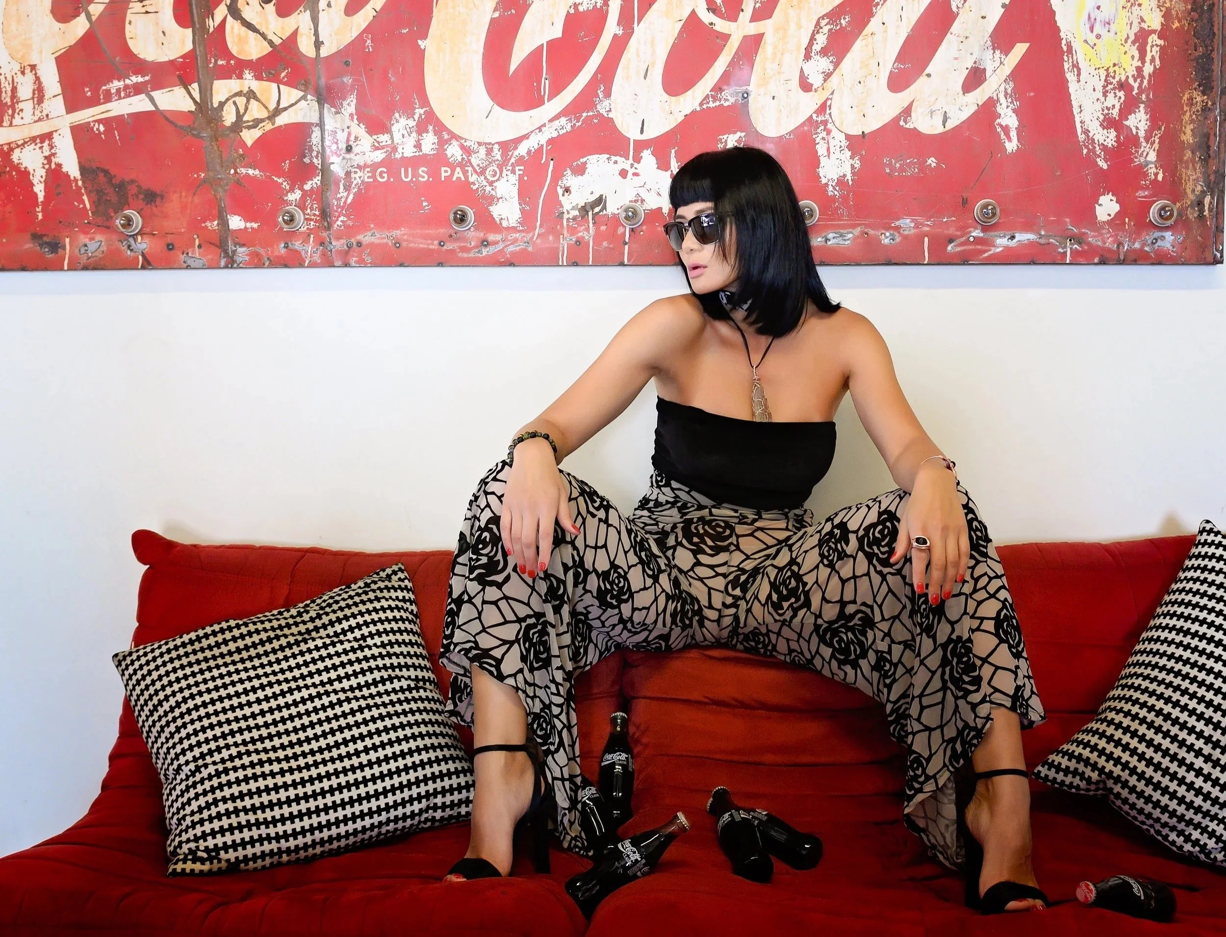 Editorial fashion portrait of a woman on a red sofa in front of a vintage Coca-Cola sign.