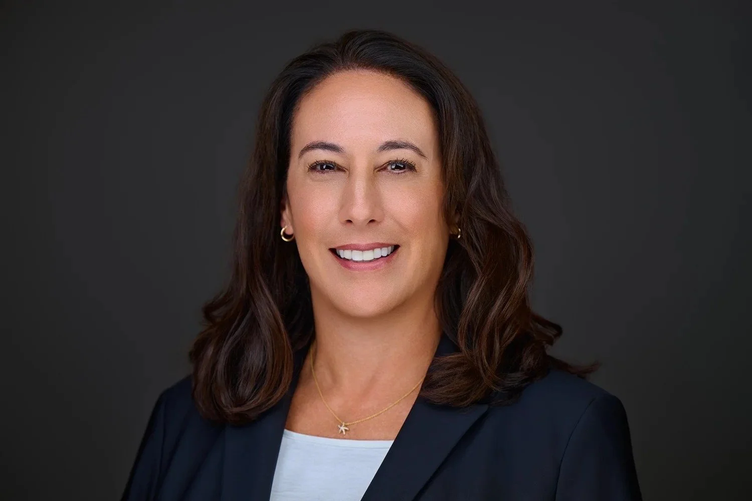 Attorney headshot of a woman in a black blazer against a dark gray studio background
