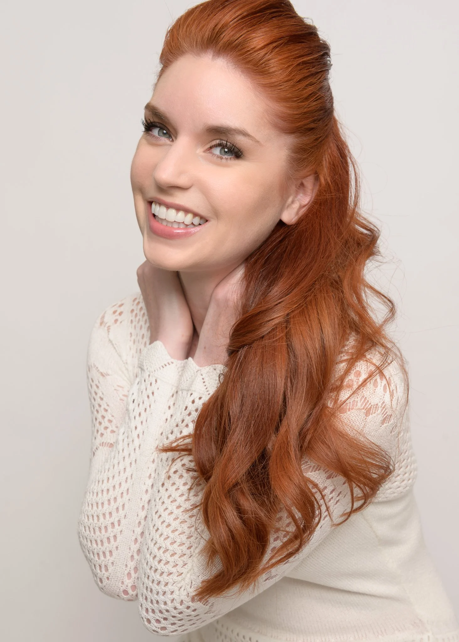 Studio portrait of a smiling woman with long red hair in a white knit sweater