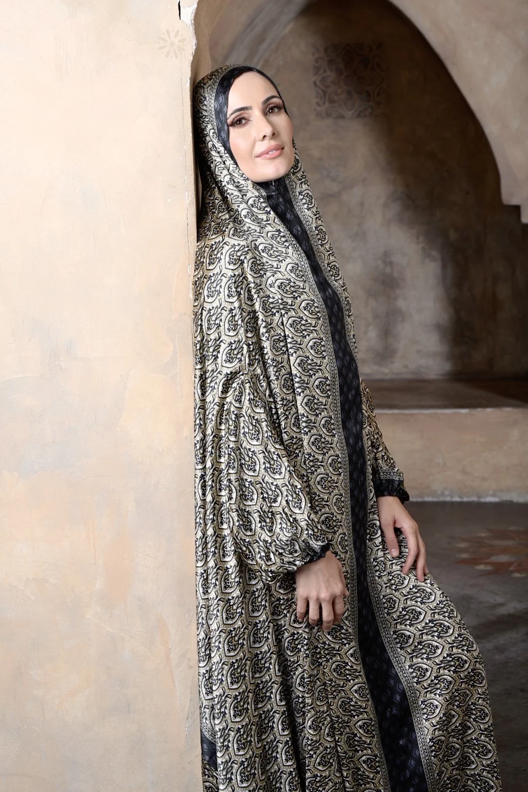 Portrait of a woman in a patterned hooded robe in a stone archway