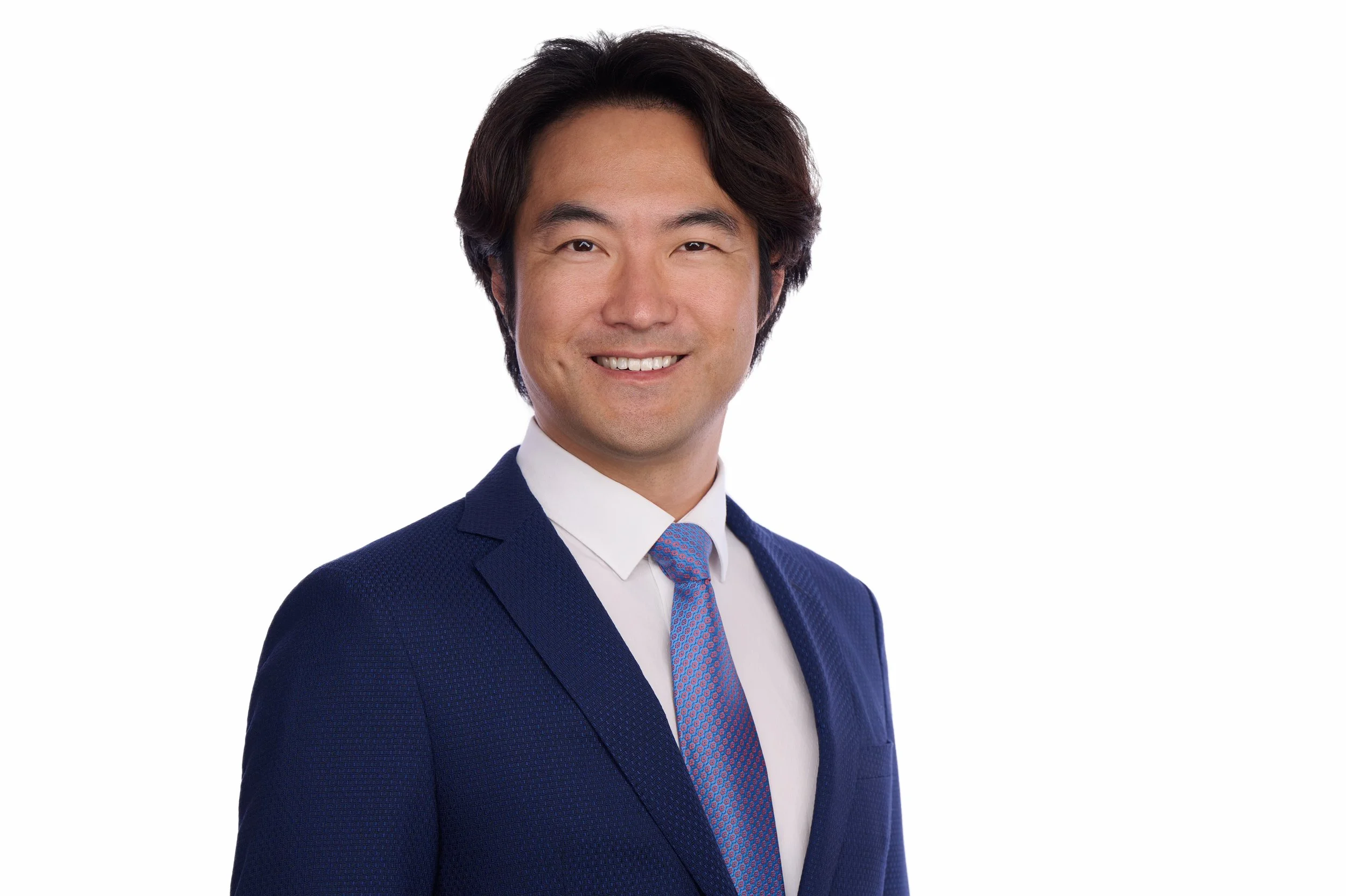 Corporate headshot of a man in a navy suit and blue tie on a white background.
