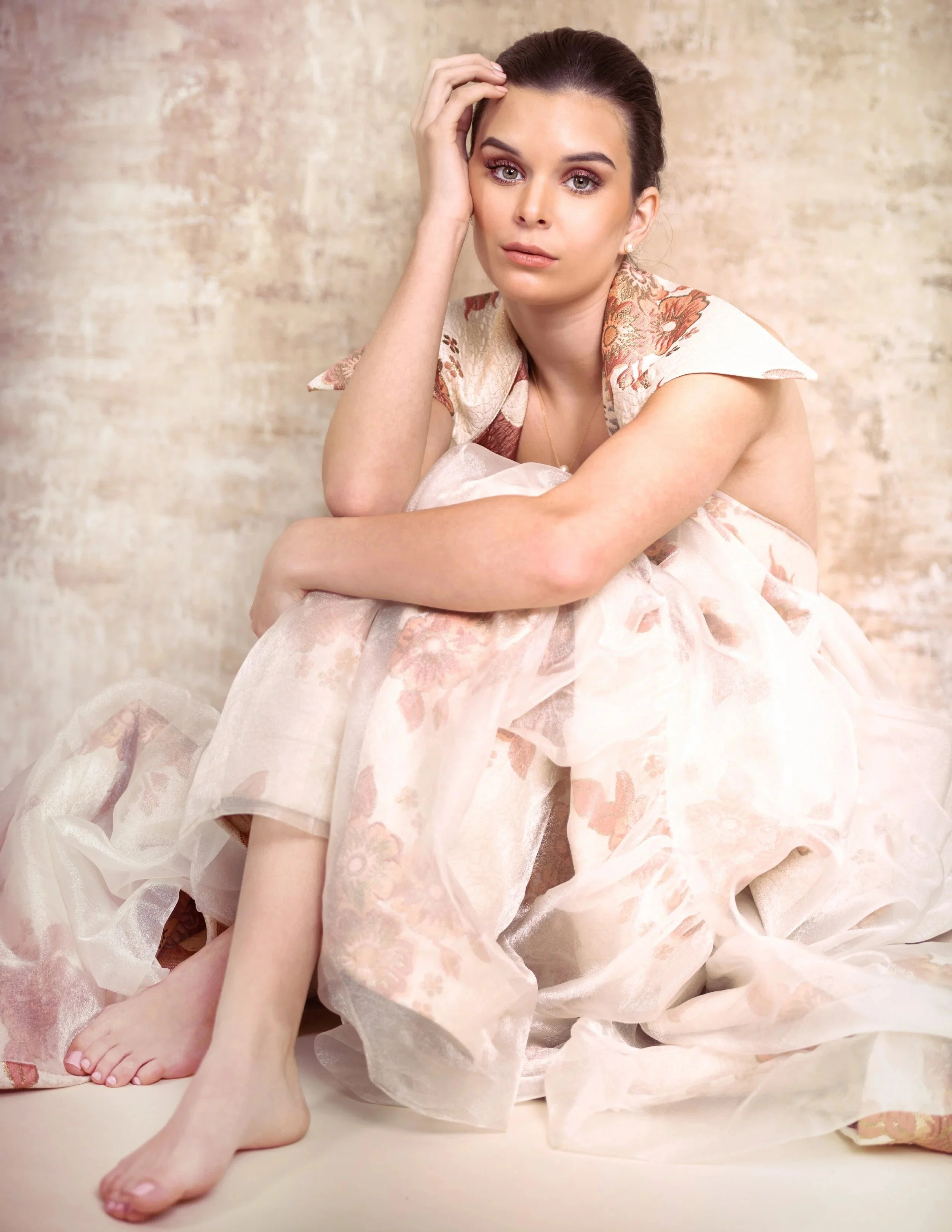 Portrait of a woman in a pale pink tulle gown seated on the floor.