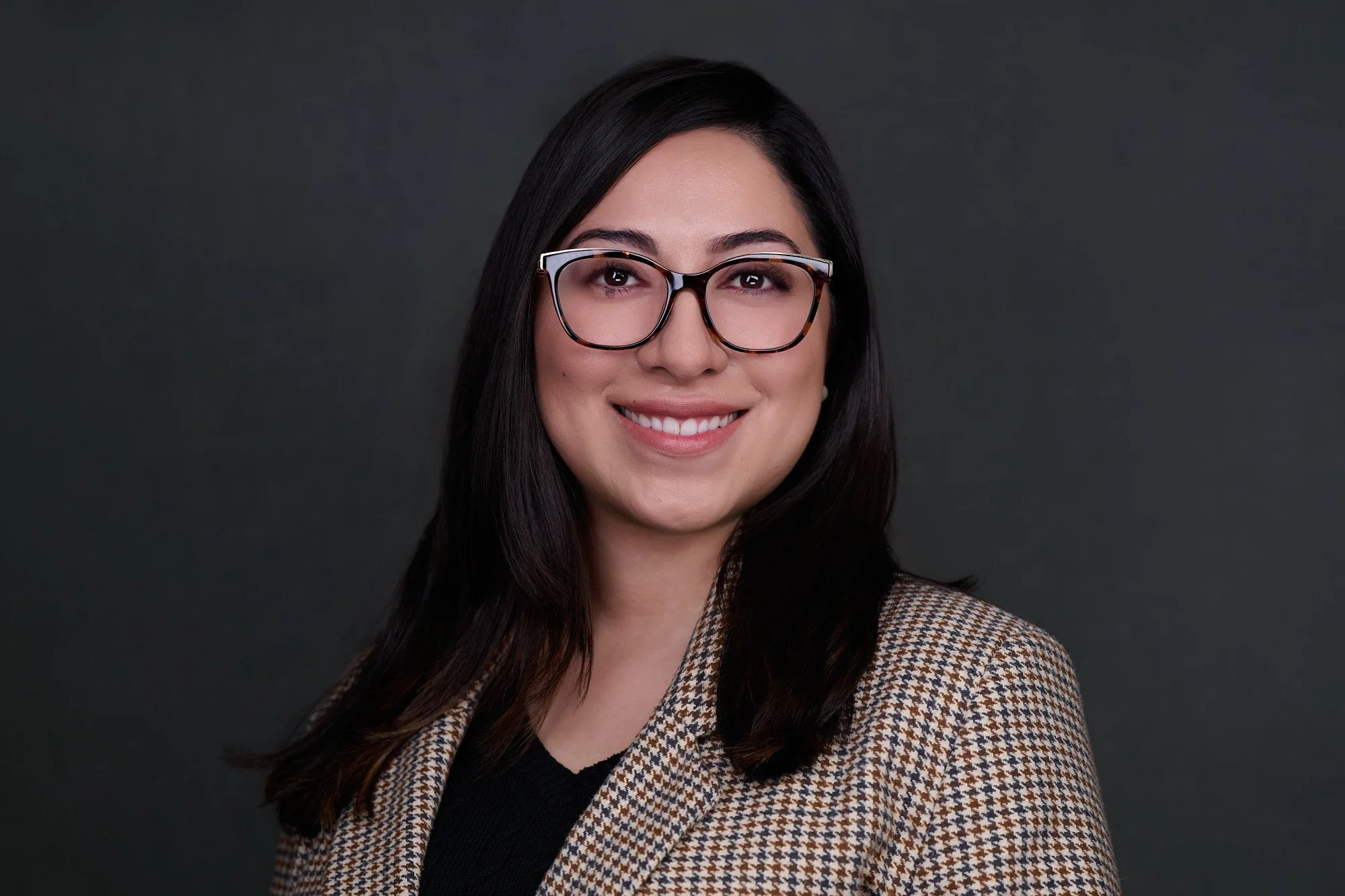 Corporate headshot of a woman with glasses in a houndstooth blazer on a charcoal backdrop, Orange County team headshot session