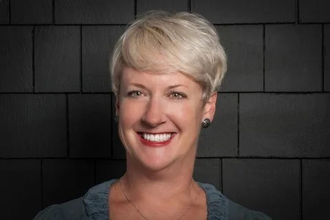 Person with short, blonde hair smiling against dark, textured background.