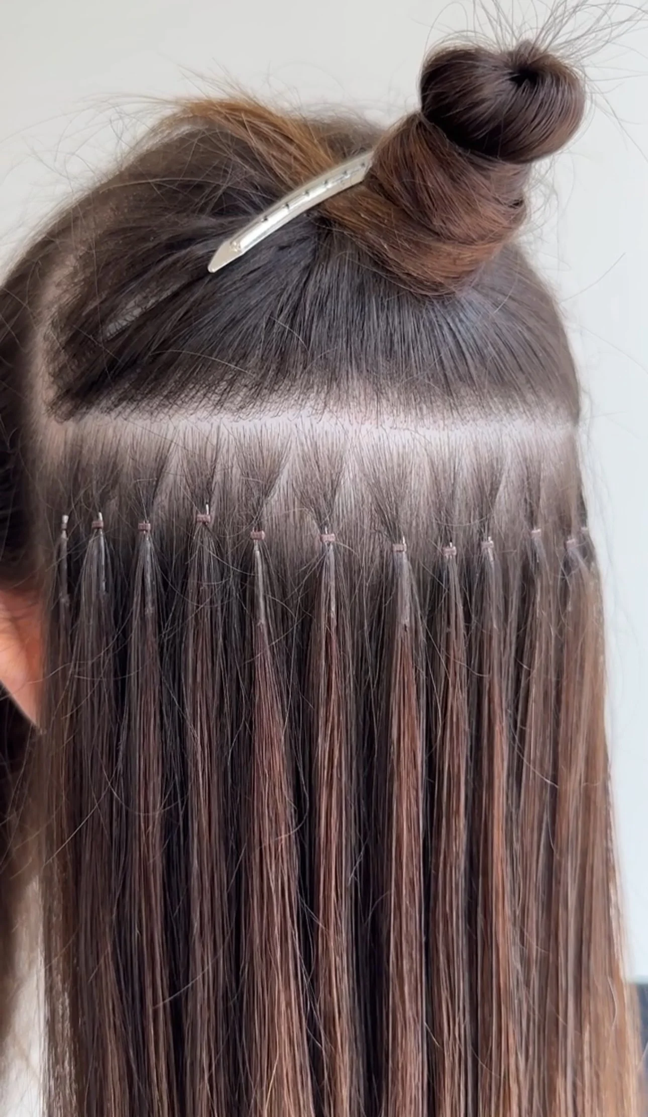 Close-up of a woman's scalp with hair extensions being installed. The natural hair is sectioned, and the extensions are bonded with small wefts attached to individual hair strands.