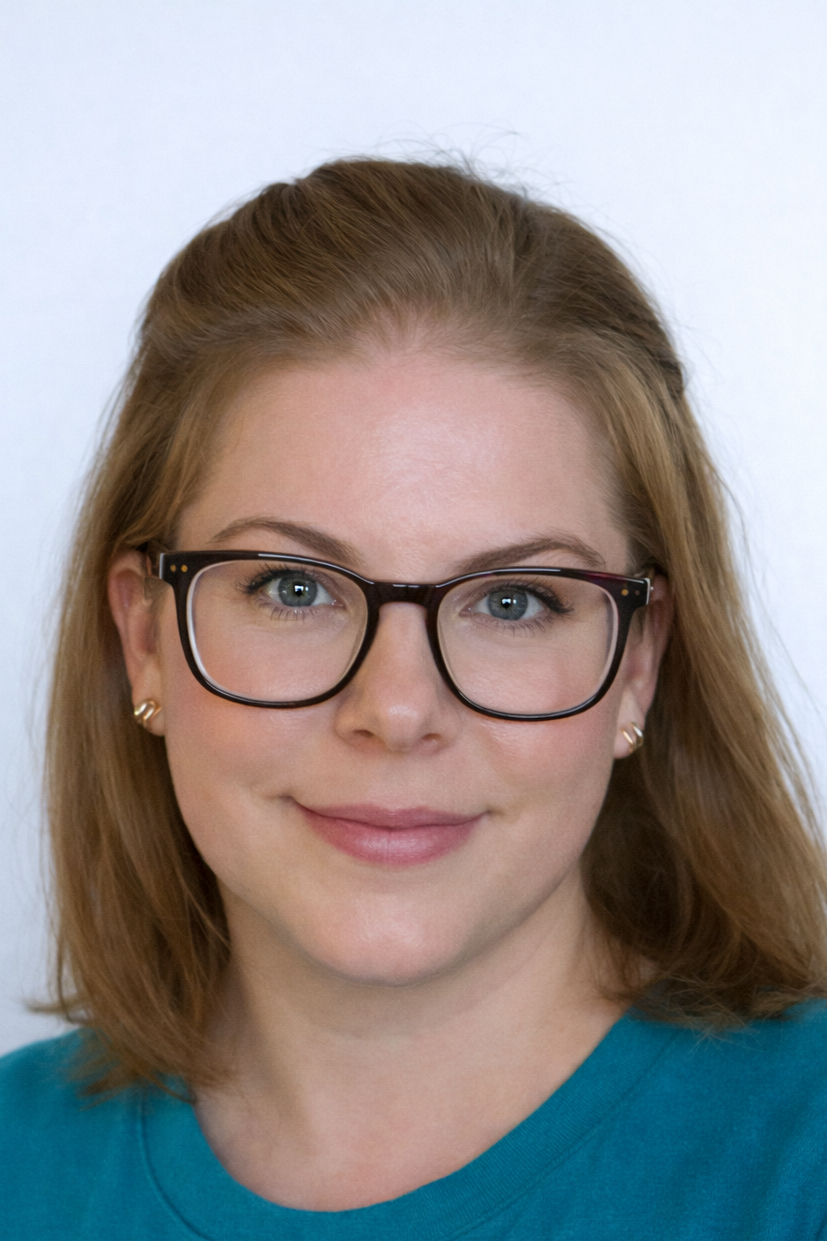 Close-up portrait of a woman with red hair, wearing glasses and a teal shirt, smiling gently.