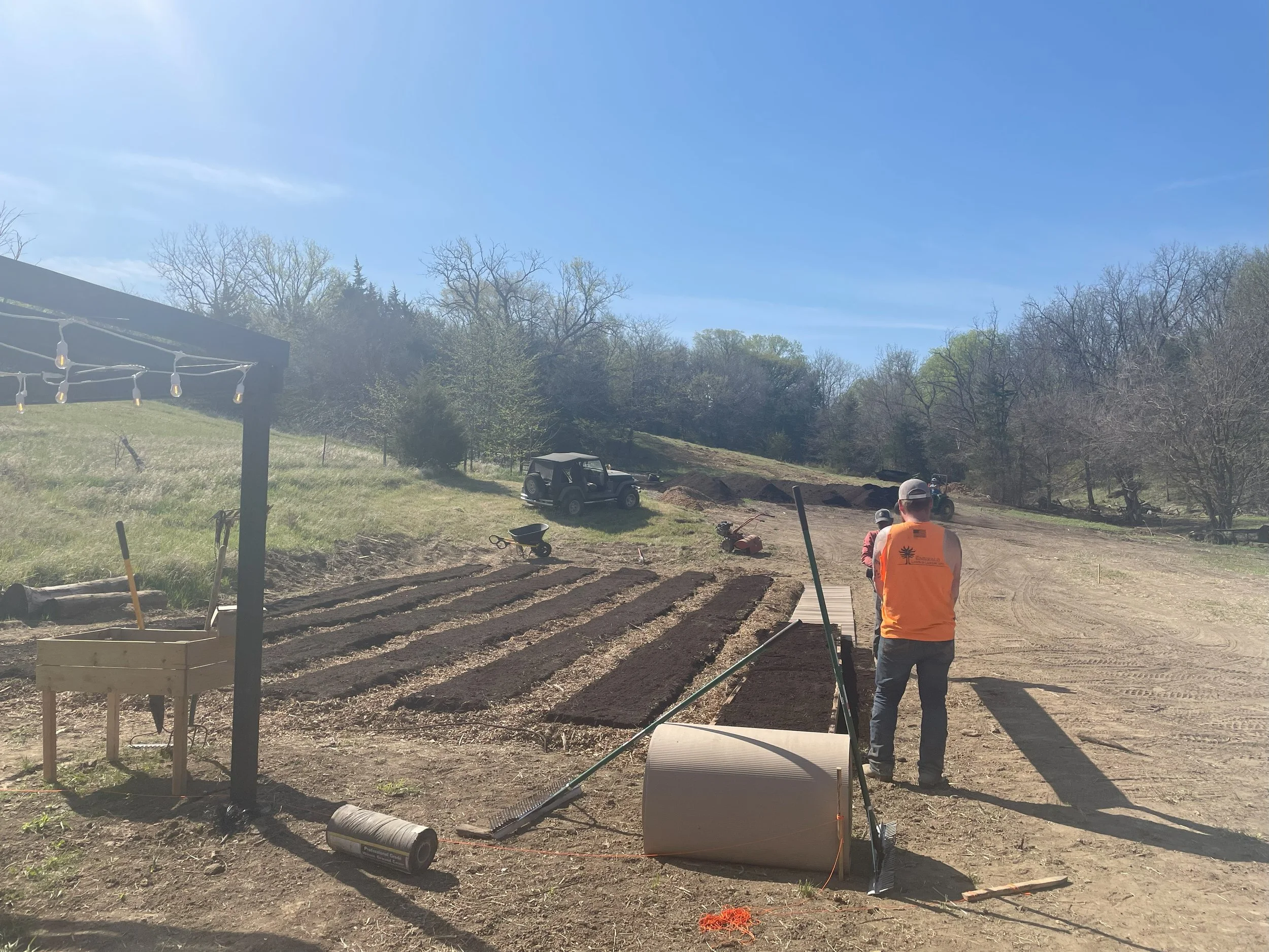 People working on a garden planting beds on a sunny day with trees in the background.