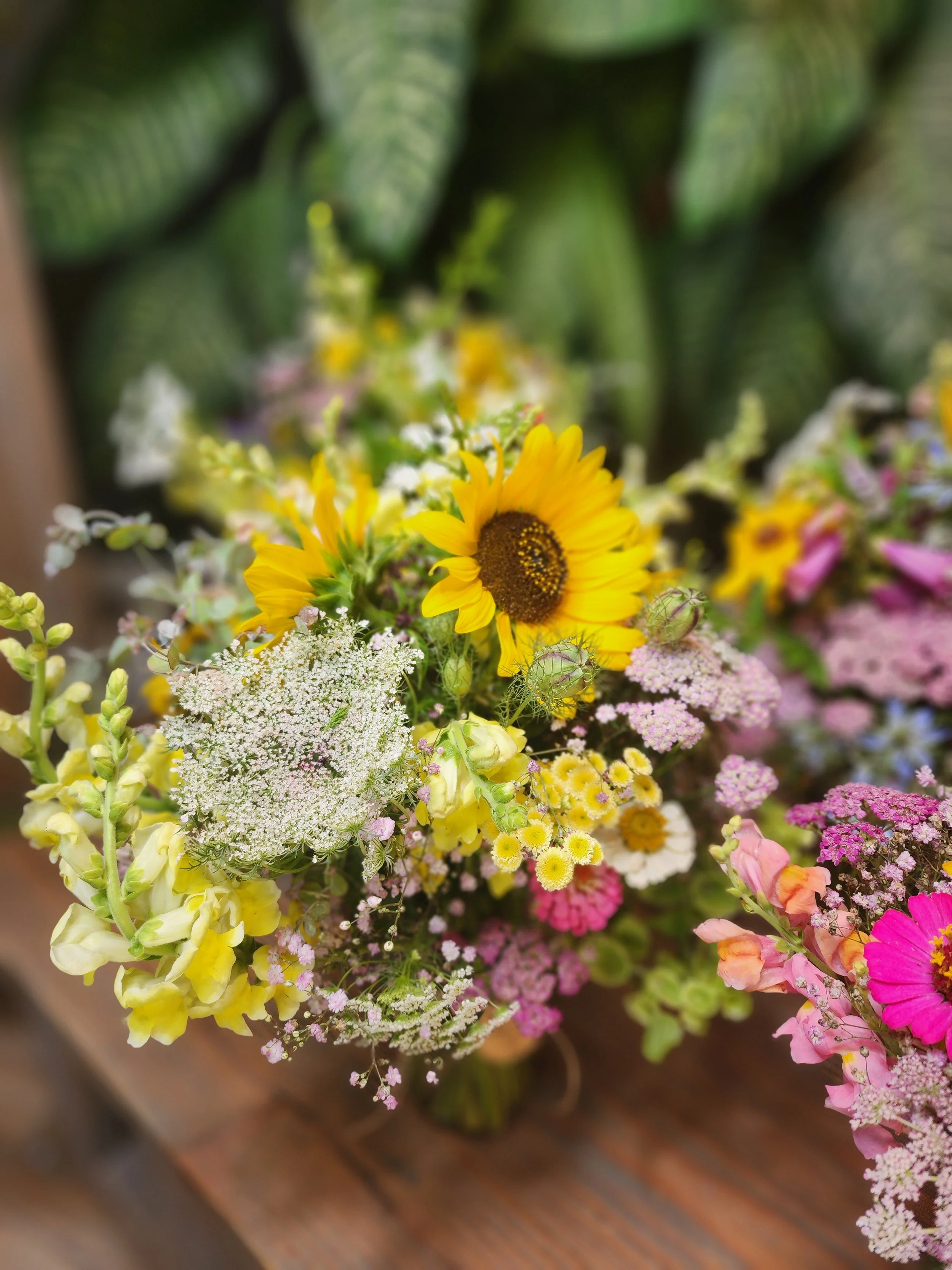 Colorful bouquet of yellow, pink, white, and purple flowers, including a sunflower, arranged on a wooden surface.