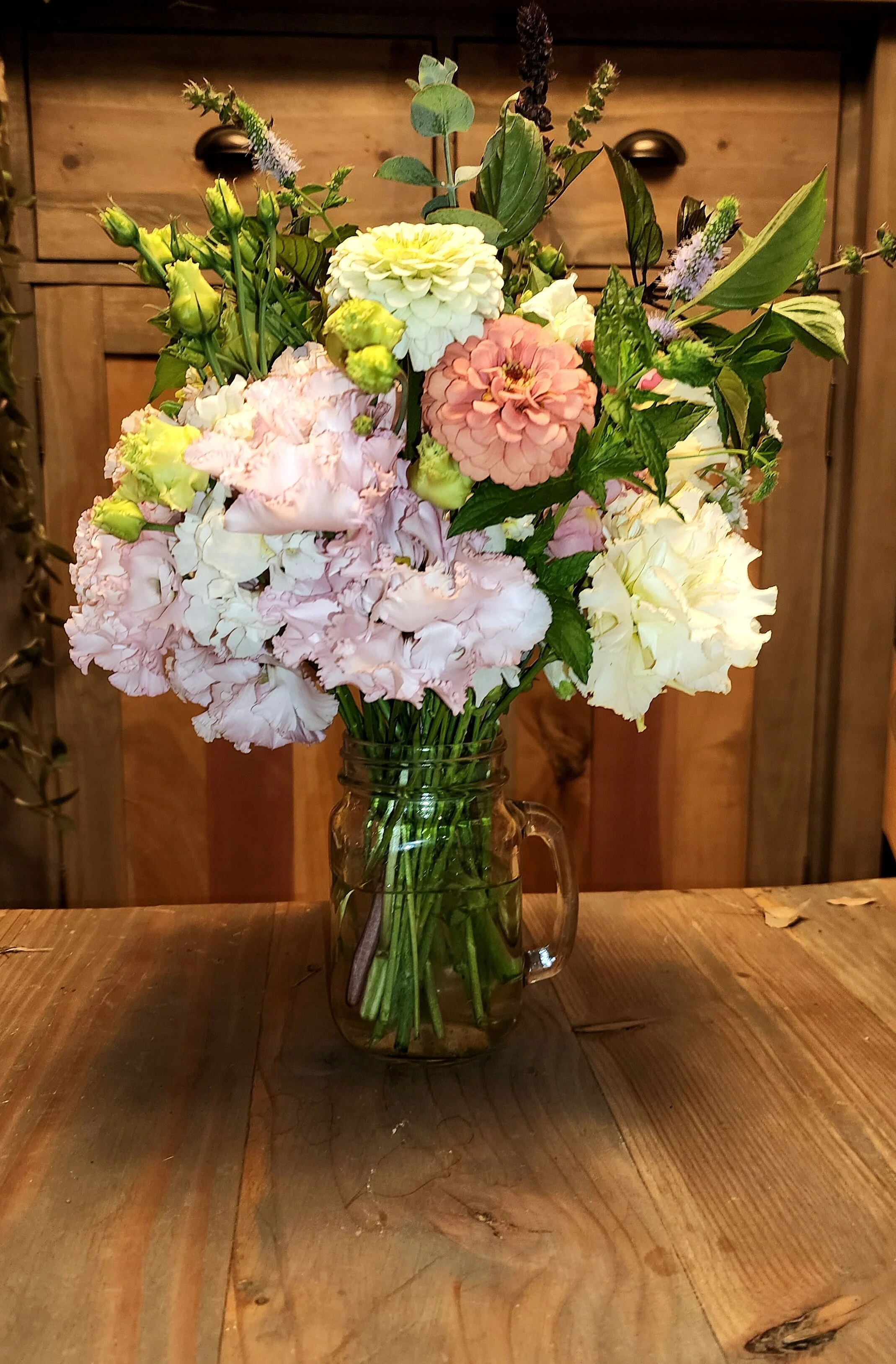 Assorted fresh flowers in a glass mason jar on a wooden table.